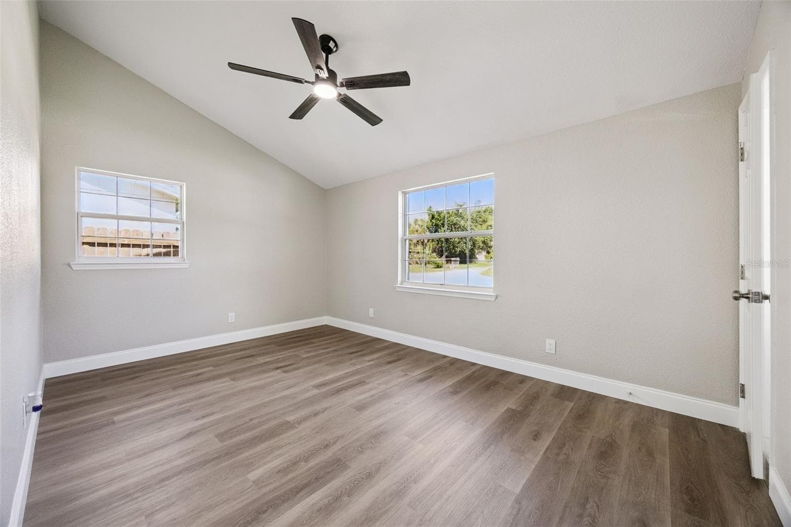 Primary Bedroom Suite: Primary bedroom featuring soaring vaulted ceilings, a modern black ceiling fan, dual windows for natural light, and low-maintenance plank flooring. - 720 GEORGIA AVE, LONGWOOD