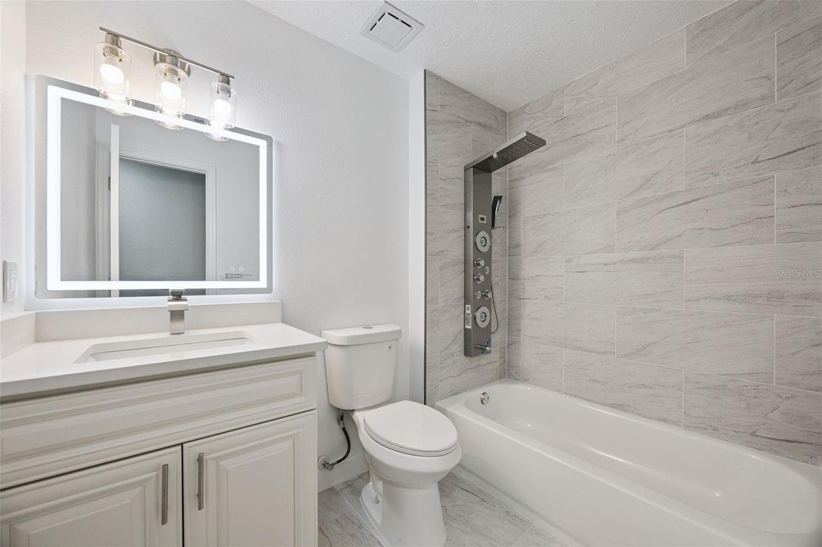 Full Guest Bathroom: Updated guest bathroom featuring a white quartz vanity, backlit LED mirror, tub/shower combination, and luxury shower tower - 720 GEORGIA AVE, LONGWOOD