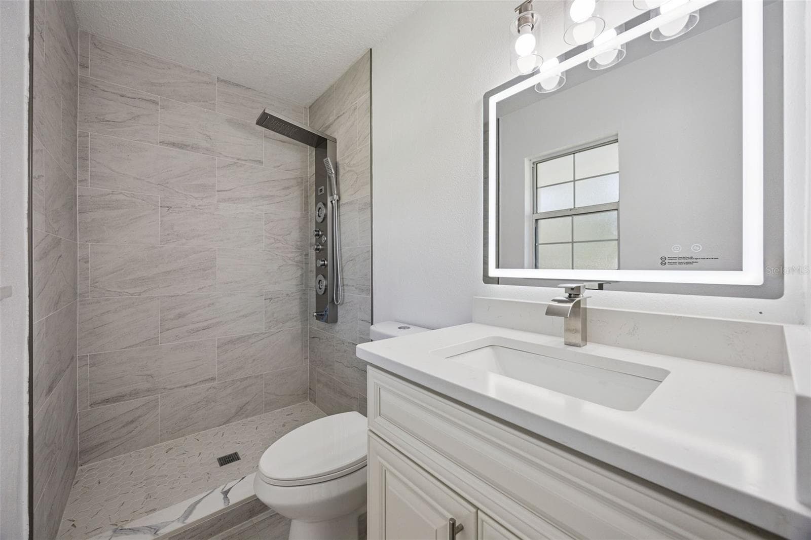 Primary Ensuite Bathroom: Modern primary bathroom complete with a white vanity, illuminated LED mirror, and tiled walk-in shower. - 720 GEORGIA AVE, LONGWOOD