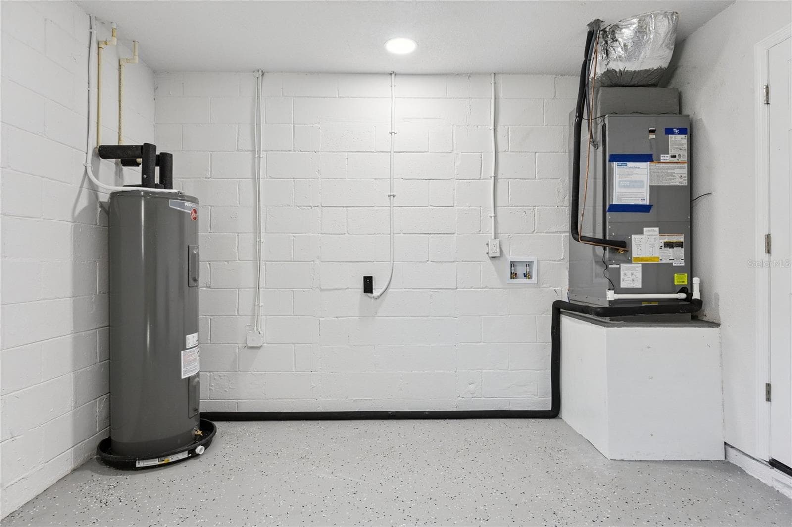 Garage & Utility Space: Clean garage utility area featuring painted concrete block walls, durable speckled epoxy flooring, water heater, and HVAC equipment. - 720 GEORGIA AVE, LONGWOOD