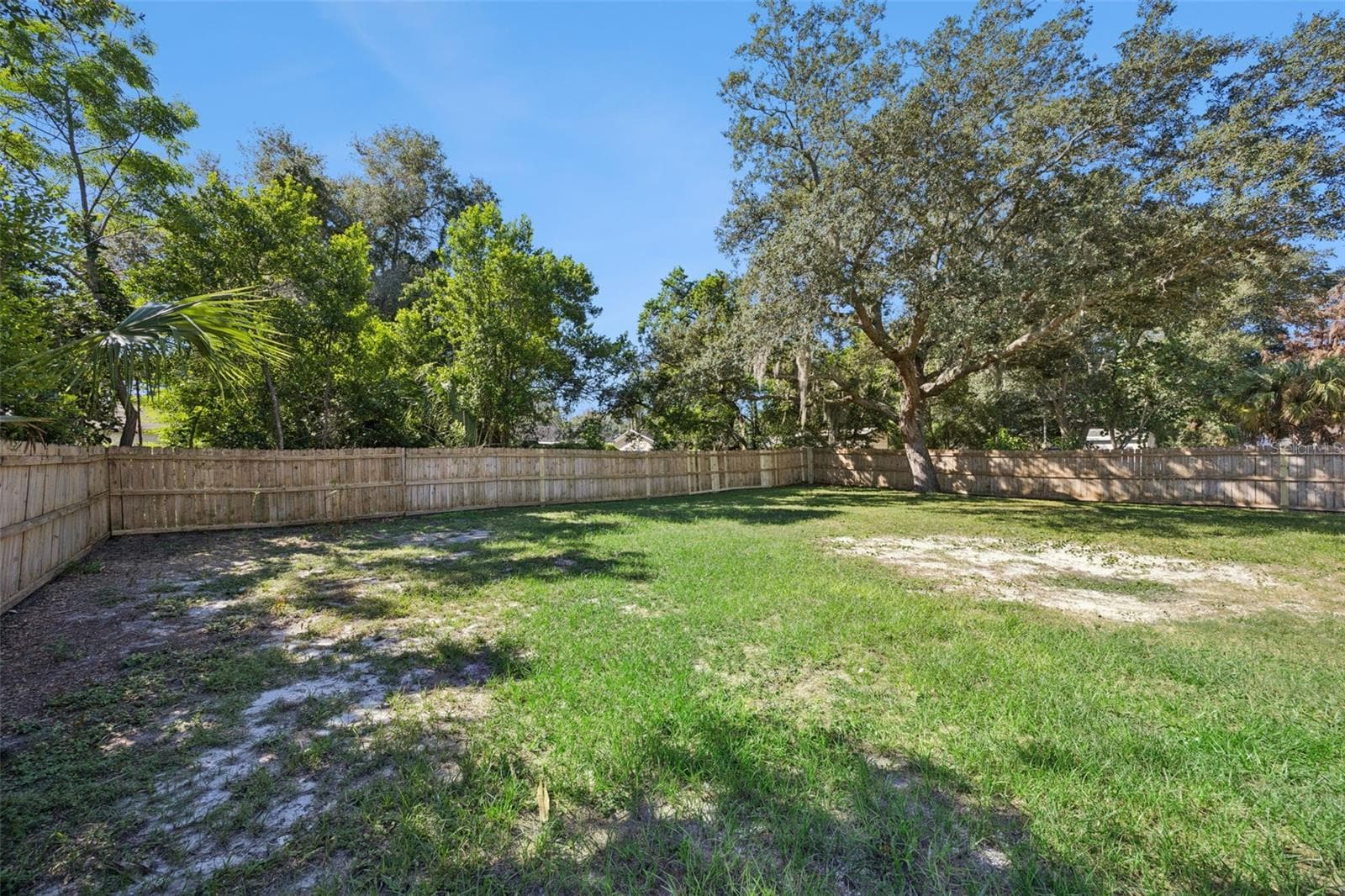 Fenced Perimeter: Clean view along the wooden privacy fence enclosure, showing the broad expanse of lawn and mature surrounding trees. - 720 GEORGIA AVE, LONGWOOD