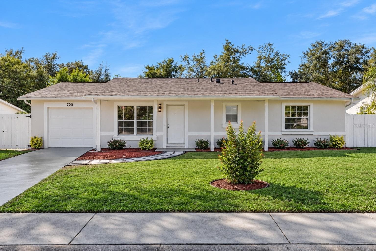 Single-Story Front Elevation: Bright front elevation of a single-story home featuring fresh light stucco, an attached single-car garage, covered front porch, and a lush, manicured lawn - 720 GEORGIA AVE, LONGWOOD