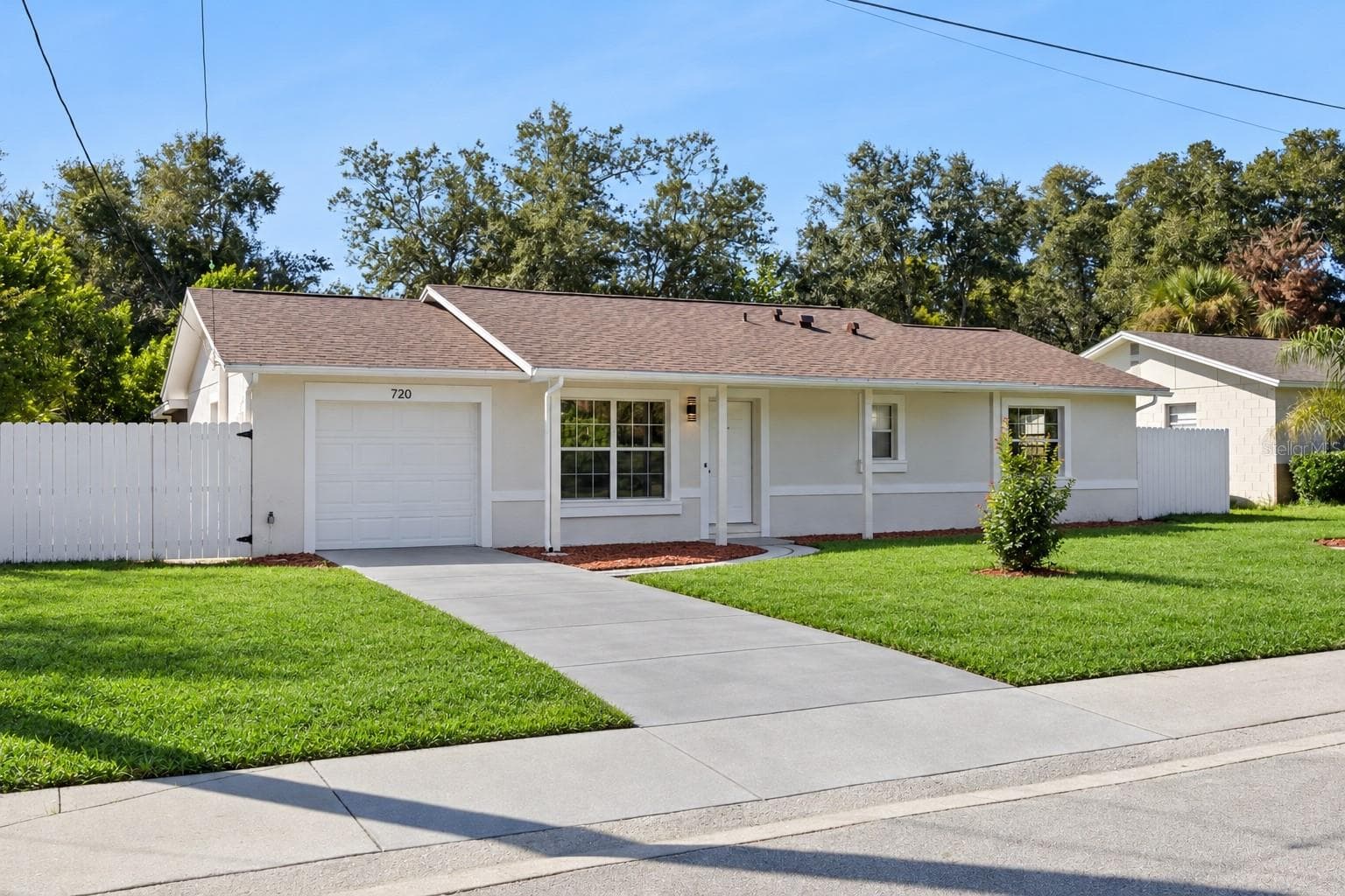 Front Exterior & Driveway: Wide street perspective showcasing the long concrete driveway, attached garage, white perimeter privacy fence, and sprawling lawn. - 720 GEORGIA AVE, LONGWOOD