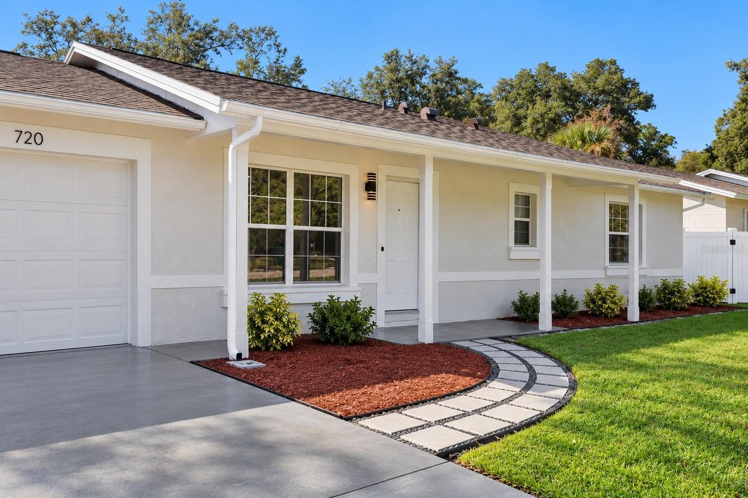 Garage & Entry Perspective: Angled front view displaying the concrete driveway leading to the attached garage, decorative paver path, and covered entry porch. - 720 GEORGIA AVE, LONGWOOD