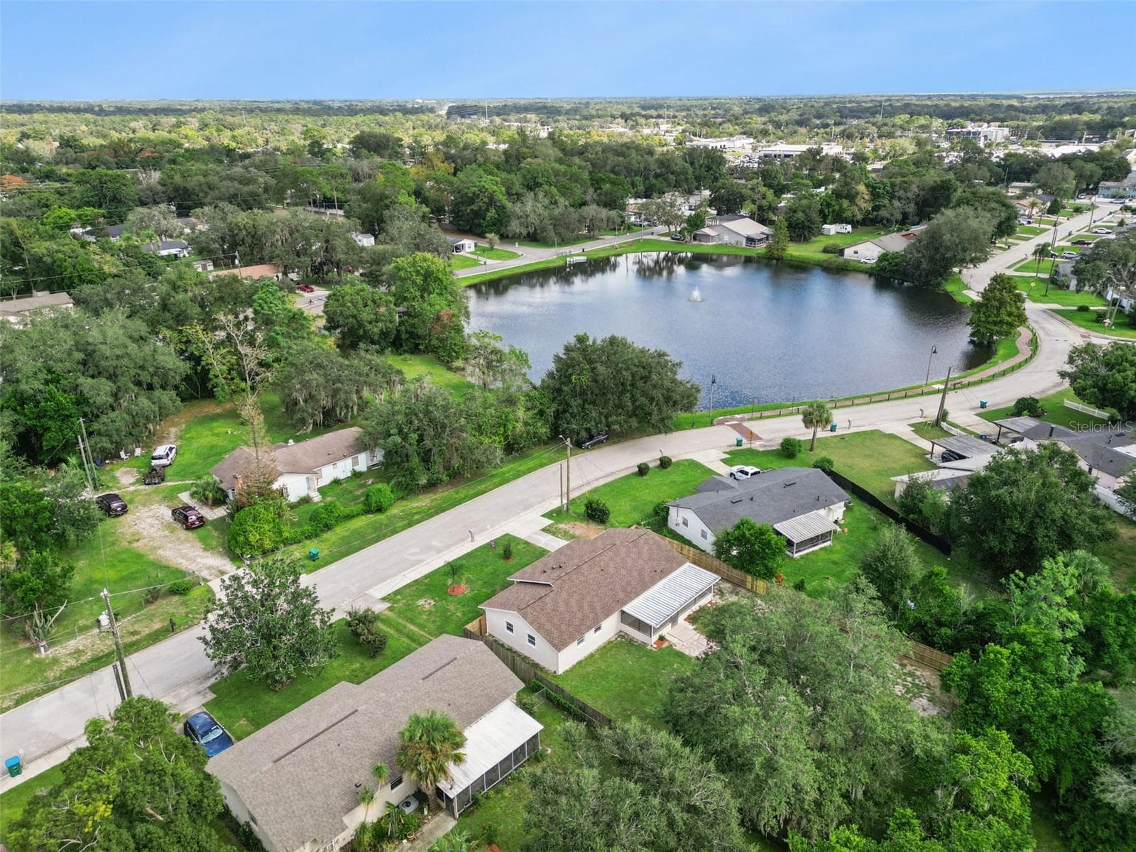 Aerial View Near Lake: High-angle aerial shot capturing the home's proximity to a scenic neighborhood lake with a central water fountain feature. - 720 GEORGIA AVE, LONGWOOD