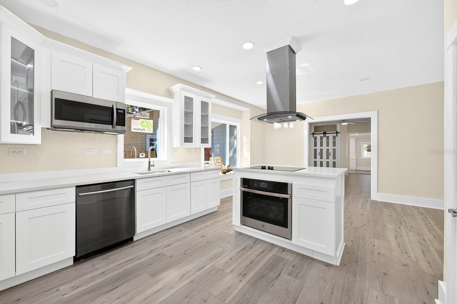 The STUNNING REMODELED KITCHEN makes a statement with crisp white cabinetry, QUARTZ COUNTERTOPS, stainless steel appliances and a center island with cooktop, built-in oven and a STRIKING CURVED GLASS RANGE HOOD. - 211 S MAPLE AVE, SANFORD