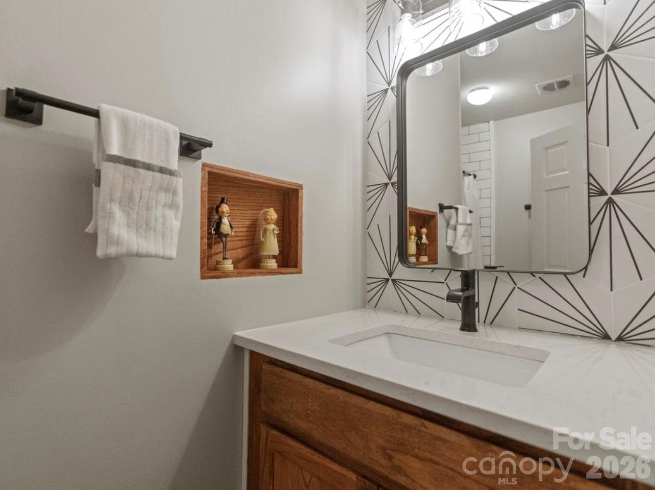 The main-level hallway bathroom has been tastefully updated with a refreshed vanity, modern mirror, updated faucet, and stylish tile backsplash, creating a clean and contemporary look. - 6626 Rocky Falls Road, Charlotte