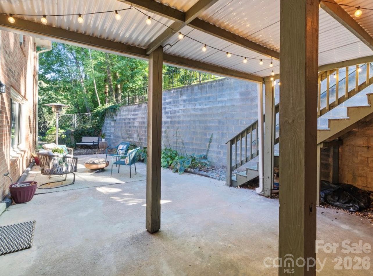 Enjoy the versatility of this covered patio, conveniently located just off the basement’s second living area and kitchen. Step outside to a quaint seating area perfect for relaxing or entertaining, with stairs leading up to the deck and convenient access to the carport. - 6626 Rocky Falls Road, Charlotte