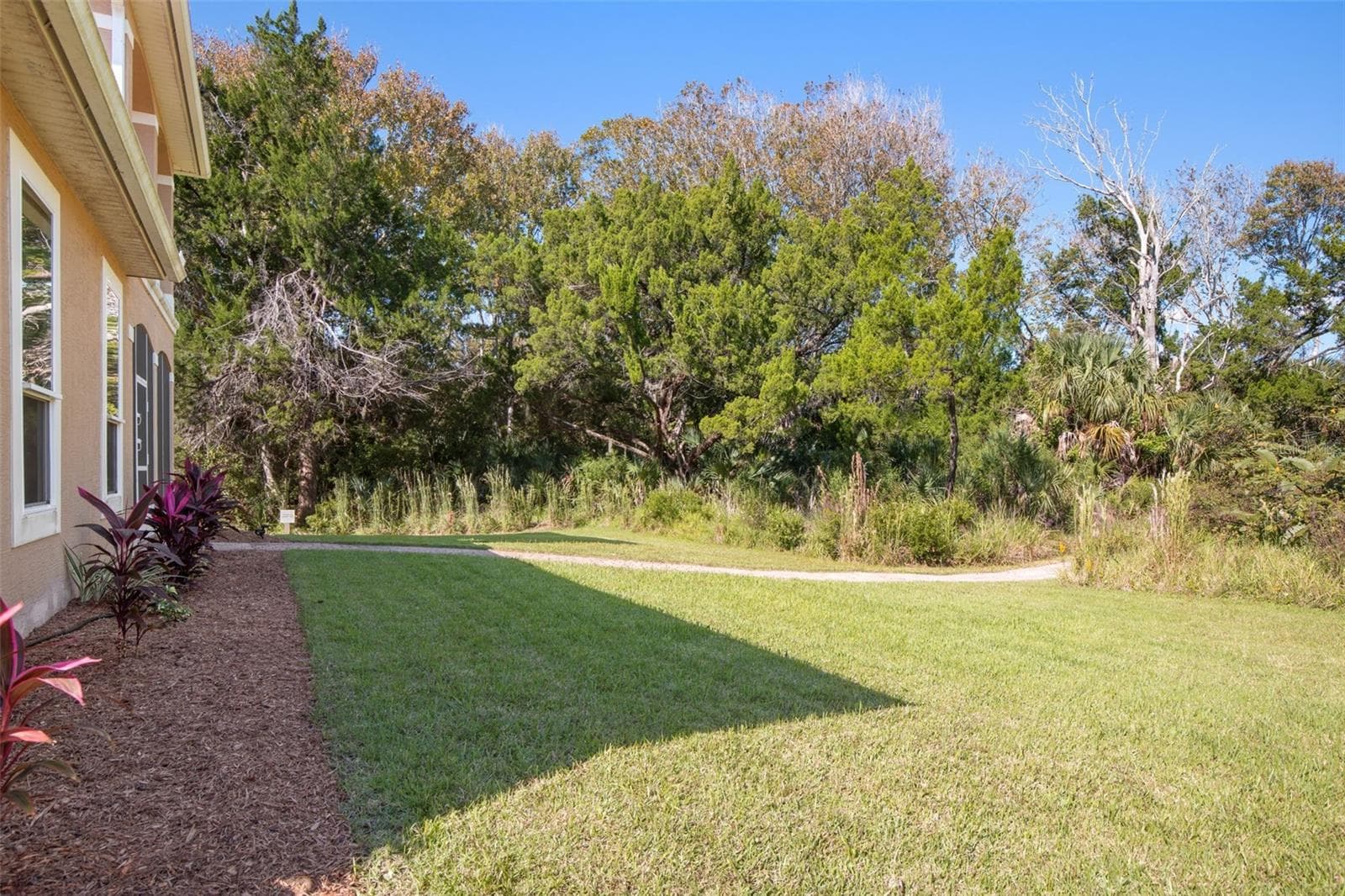 Peaceful backyard surrounded by natural greenery with a walkway leading toward Emerald Lake. - 25 EMERALD LAKE CT, PALM COAST