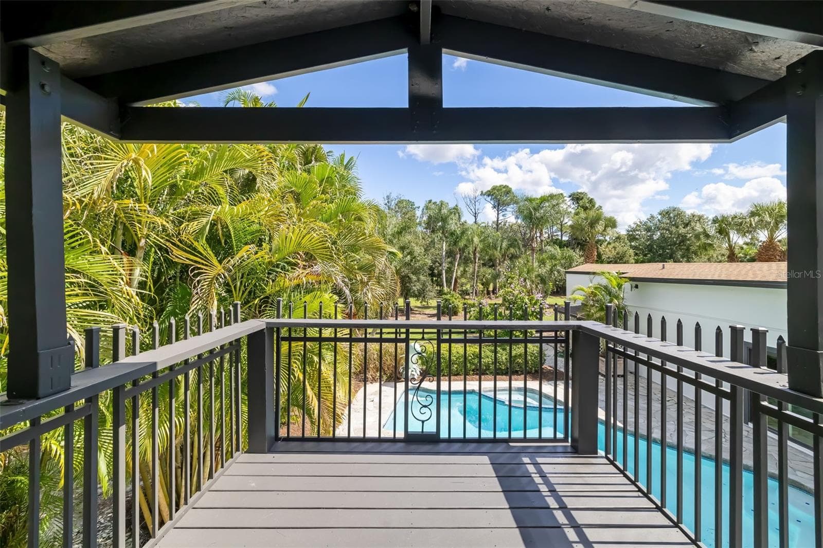 Second-floor primary bathroom opens to a private covered balcony with relaxing views over the pool and surrounding tropical landscape. - 403 LONGBOW TRL, OSPREY