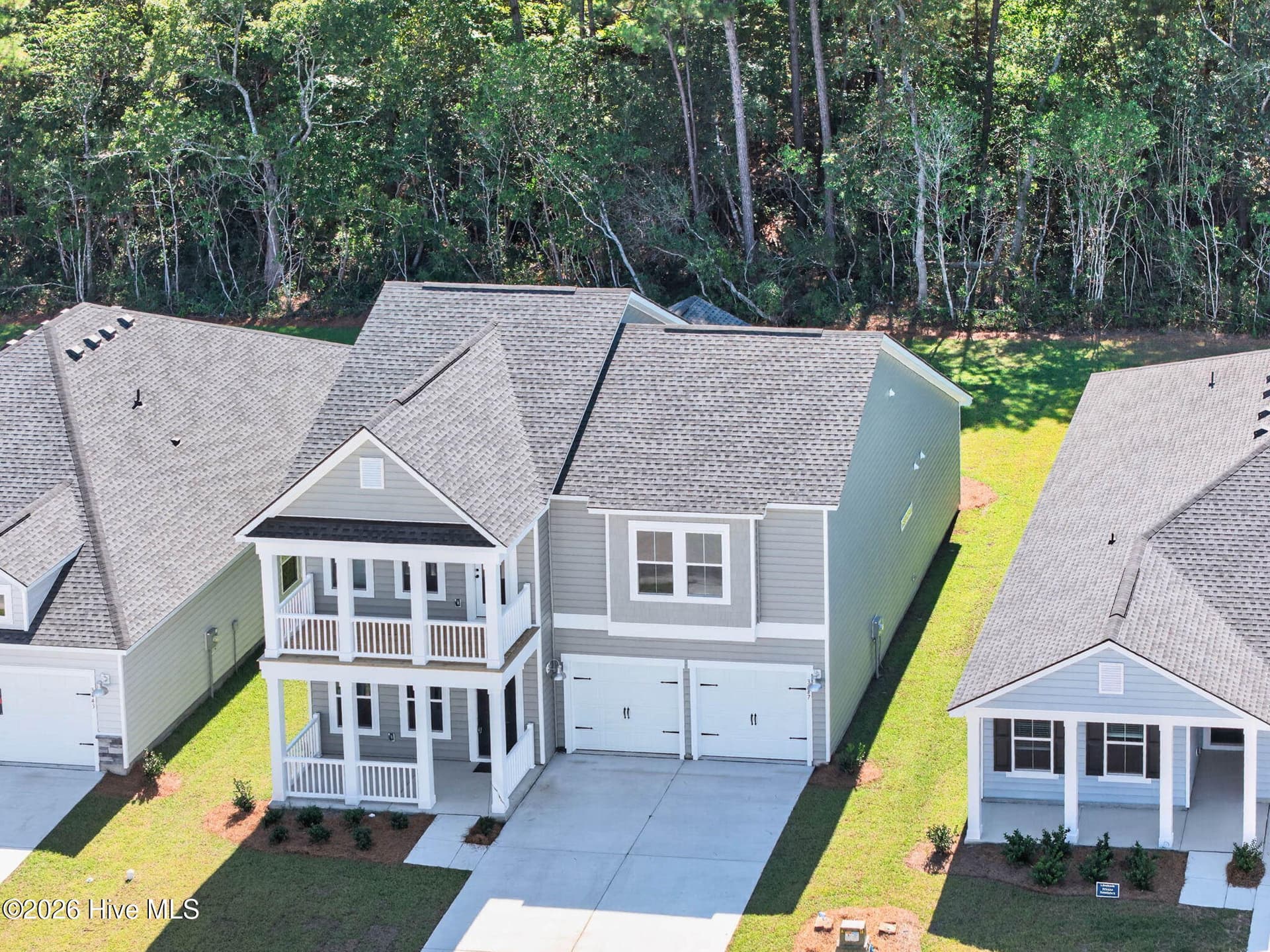 Angled aerial view highlighting the covered front porch, second-floor balcony, and attached two-car garage. - 3447 Sandhill Crane Drive SW, Ocean Isle Beach, NC 28469
