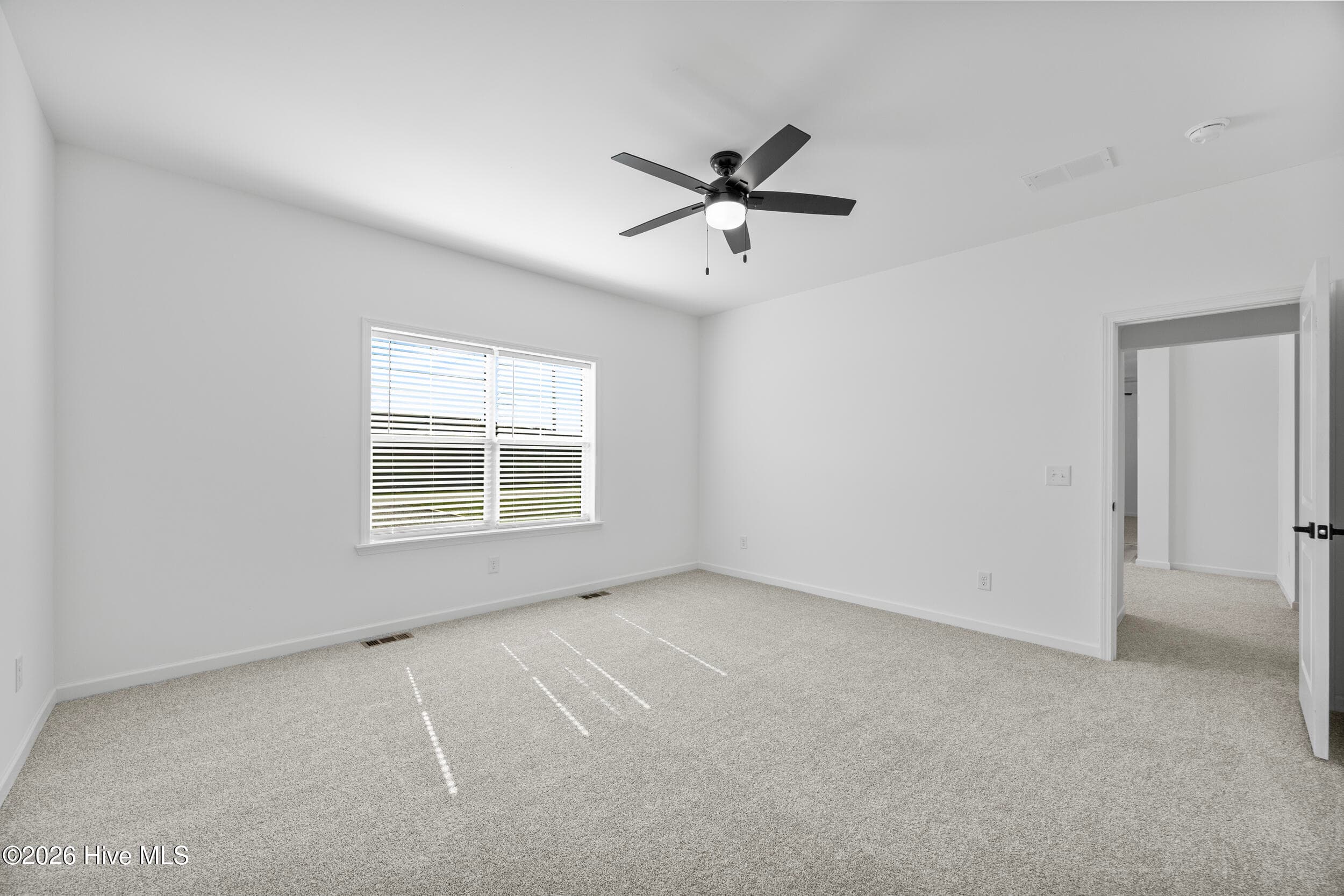 Spacious primary bedroom featuring soft neutral tones, plush carpeting, abundant natural light and a stylish ceiling fan. A bright and inviting retreat with plenty of room to relax and unwind - 771 Factory Road, Hampstead, NC 28443