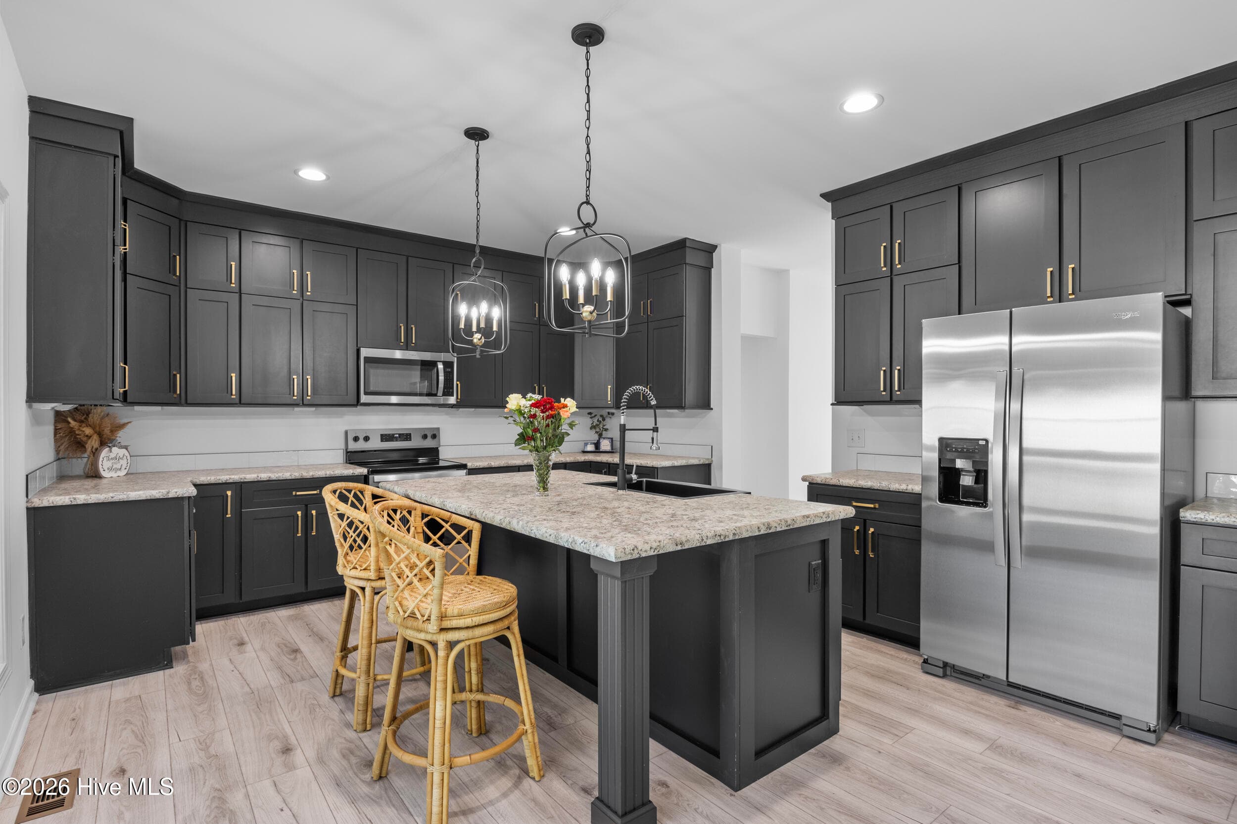 Beautifully designed kitchen featuring rich dark cabinetry, sleek countertops, stainless steel appliances, and a spacious center island with breakfast bar seating. Stylish pendant lighting and an open layout create an inviting space perfect for everyday living and entertaining - 771 Factory Road, Hampstead, NC 28443