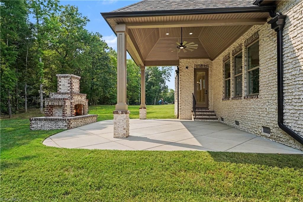 This property features a covered patio under a hip roof, equipped with an oversized ceiling fan and a custom brick fire pit, perfect for outdoor entertaining. - 1477 Cappoquin Way, Burlington NC 27215, Burlington