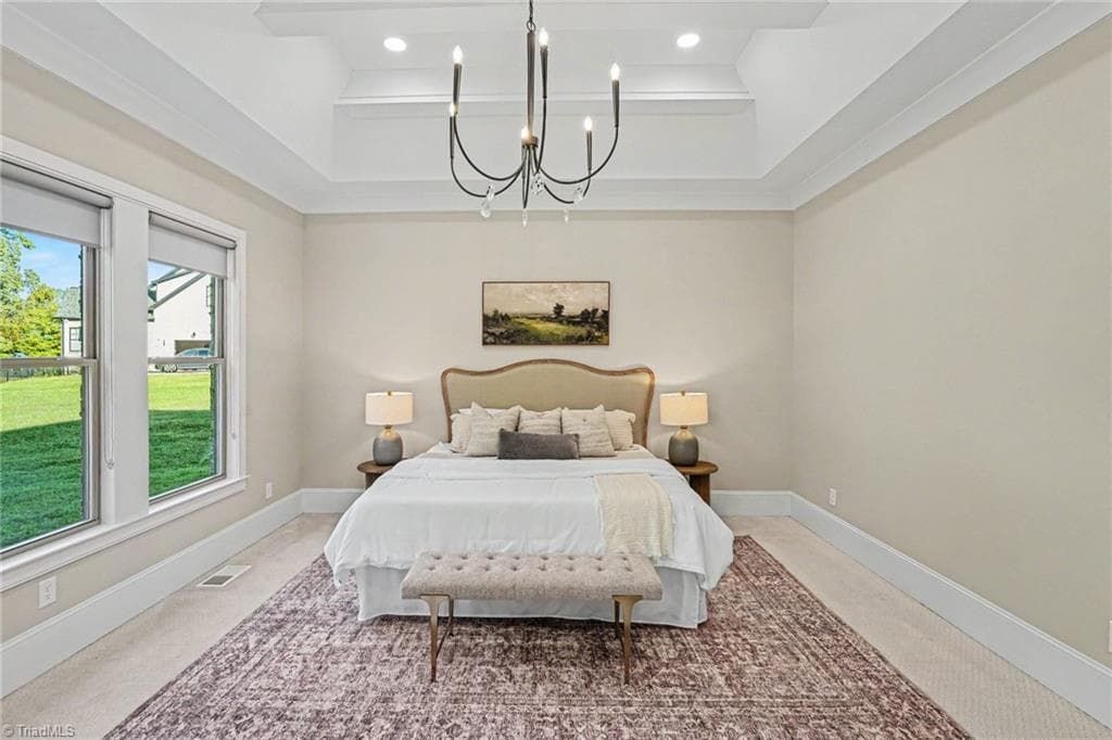 Primary bedroom ensuite featuring a detailed ceiling, elegant chandelier, large windows, and plush carpeting. - 1477 Cappoquin Way, Burlington NC 27215, Burlington