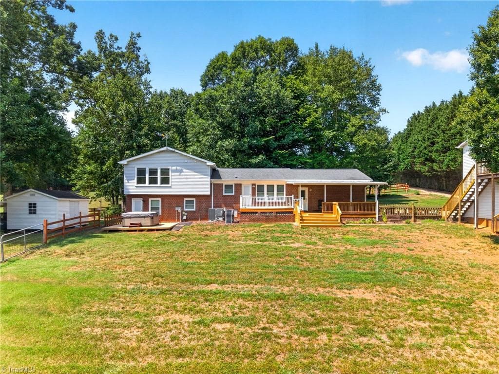 The back of this 1994 built split level home features a lower porch with a hot tub and large porch with covered section. To the left is a large storage building with 2 space carport. To the right of the home is a 2 car garage with unfinished in-law suite above the 2 car garage. - 8546 Hudson-James Road, Summerfield NC 27358, Summerfield