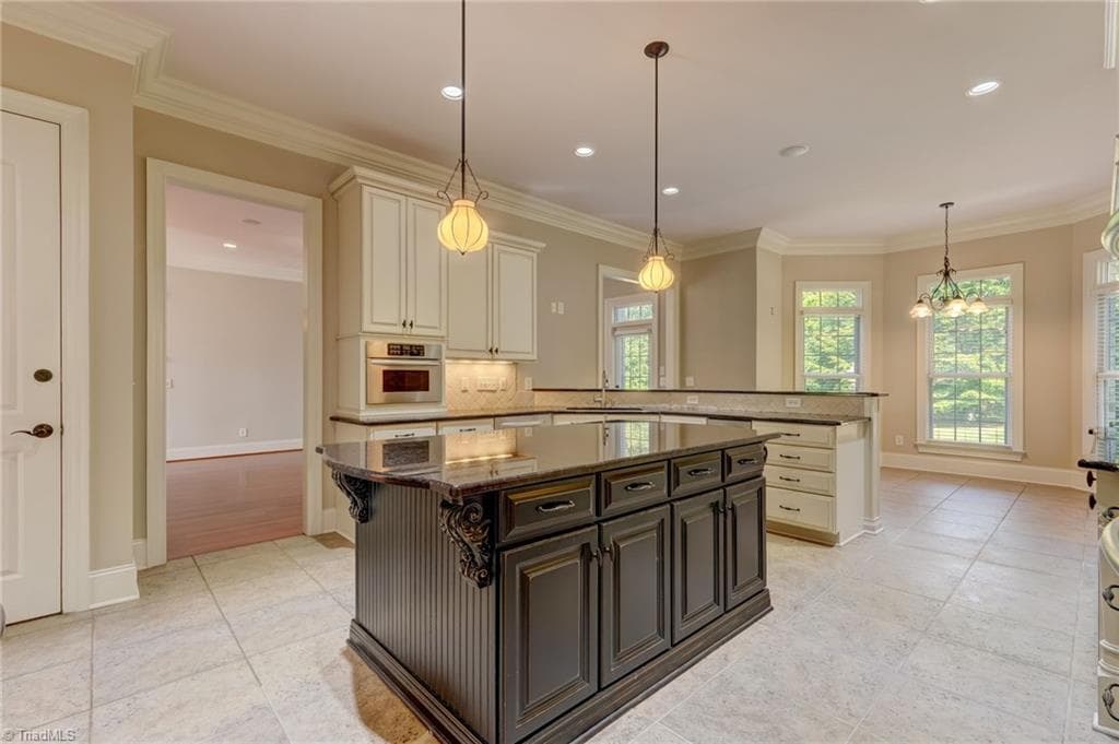 A beautifully appointed gourmet kitchen featuring double ovens, large island, elegant granite countertops, a premium gas cooktop, sophisticated under-cabinet lighting, and a convenient built-in trash compactor. - 4404 Liguria Court, Summerfield NC 27358, Summerfield