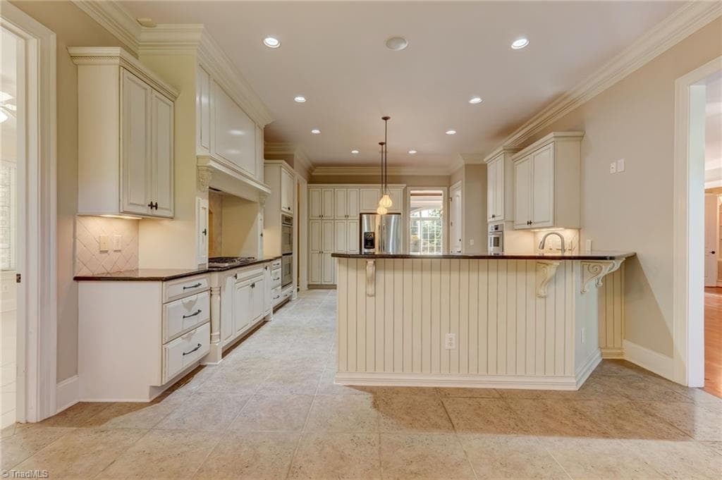 A beautifully appointed gourmet kitchen featuring double ovens, large island, elegant granite countertops, a premium gas cooktop, sophisticated under-cabinet lighting, and a convenient built-in trash compactor. - 4404 Liguria Court, Summerfield NC 27358, Summerfield