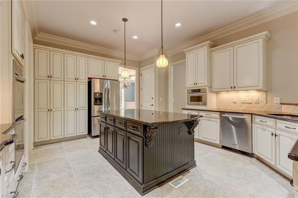 A beautifully appointed gourmet kitchen featuring double ovens, large island, elegant granite countertops, a premium gas cooktop, sophisticated under-cabinet lighting, and a convenient built-in trash compactor. - 4404 Liguria Court, Summerfield NC 27358, Summerfield