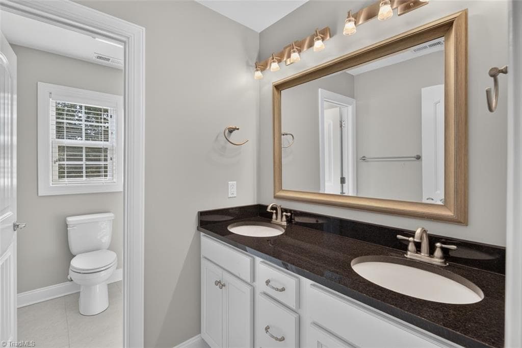 Upstairs hall bathroom w/double vanity, granite counters, and neutral tile. - 7807 Winterbourne Drive, Summerfield NC 27358, Summerfield