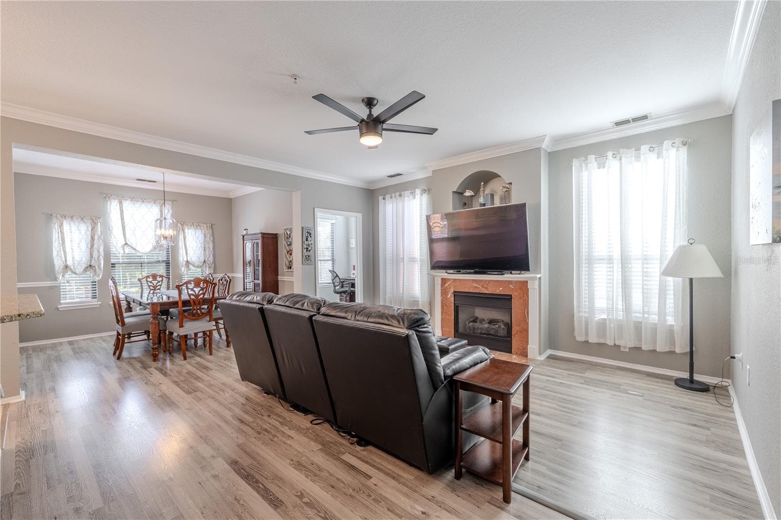 Another view of this inviting living area is anchored by a gas fireplace with a classic mantle and decorative niche above, flanked by tall windows with sheer curtains that fill the space with soft, natural light. - 2738 VIA TIVOLI #220B, CLEARWATER