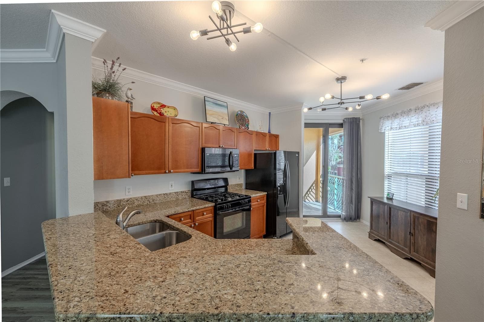 An expansive granite breakfast bar anchors the kitchen, complemented by warm wood cabinetry, stainless appliances, and an open sightline to the foyer and living areas for effortless entertaining. - 2738 VIA TIVOLI #220B, CLEARWATER