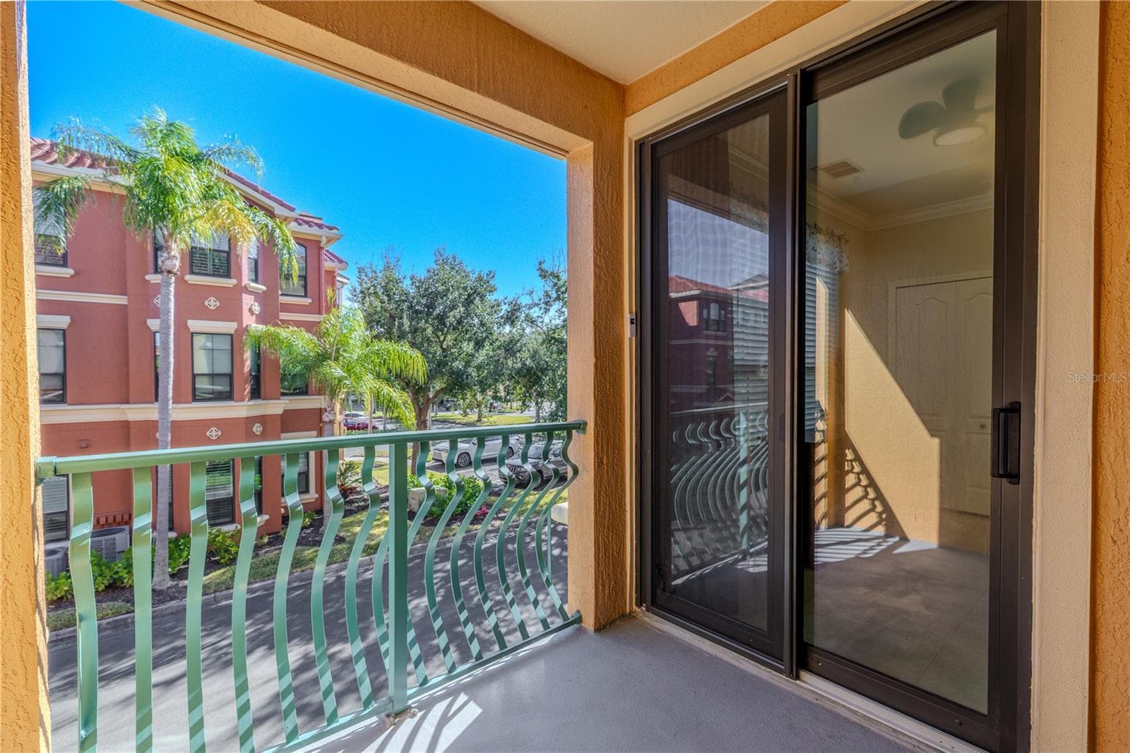 Private covered balcony with sliding glass doors, offering a sunny outdoor space and elevated views of the palm-lined community streetscape. - 2738 VIA TIVOLI #220B, CLEARWATER