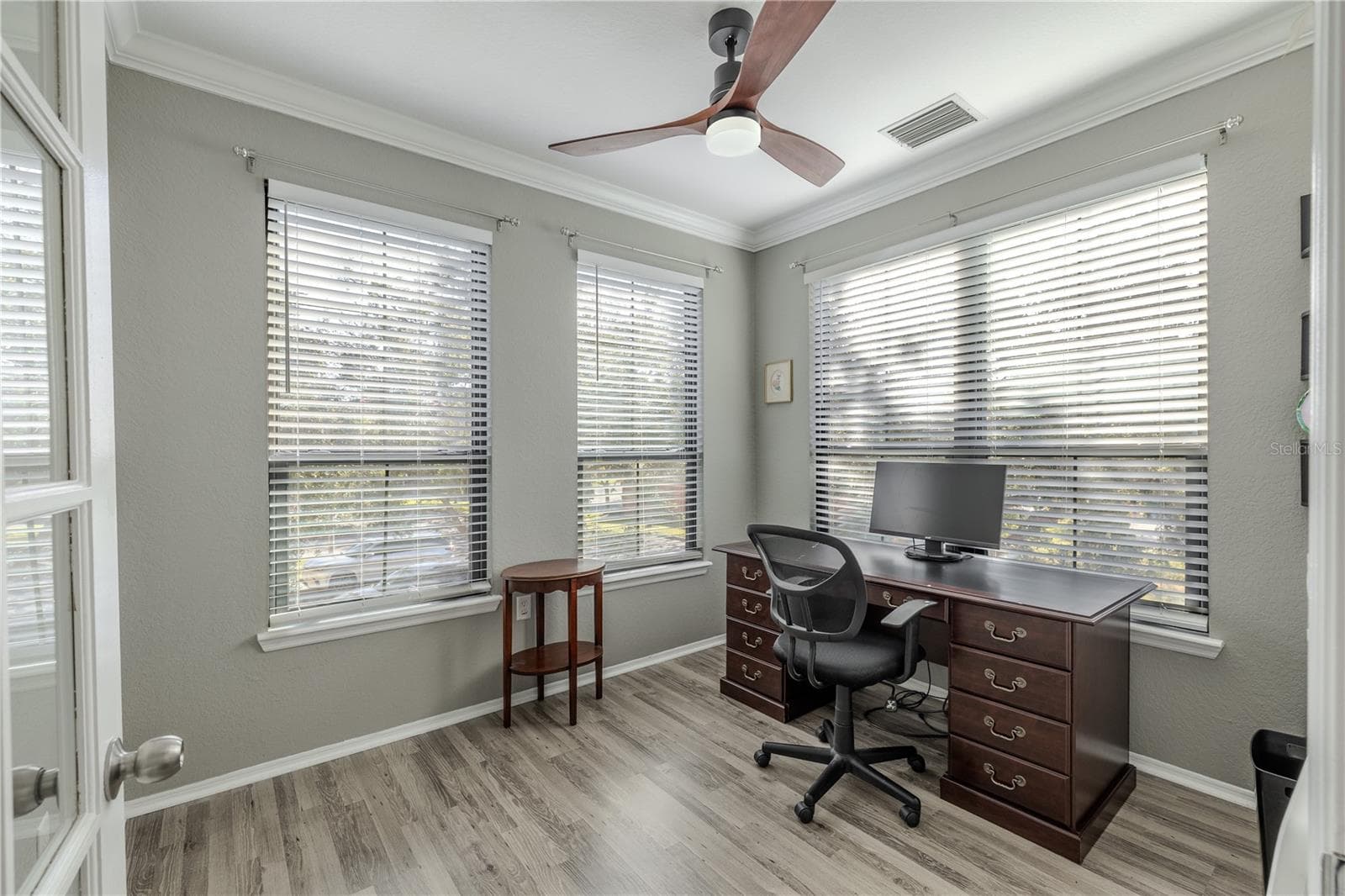Bright flex room/home office with crown molding, modern ceiling fan, and wraparound windows that fill the space with natural light, complemented by updated flooring. - 2738 VIA TIVOLI #220B, CLEARWATER