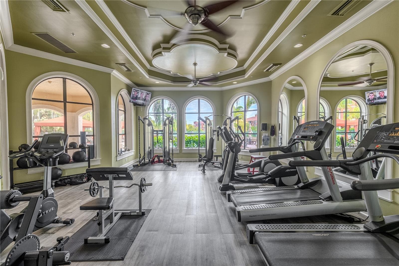 Spacious clubhouse fitness center with cardio and strength equipment, soaring tray ceilings, and tall arched windows that flood the gym with natural light and resort-style views. - 2738 VIA TIVOLI #220B, CLEARWATER