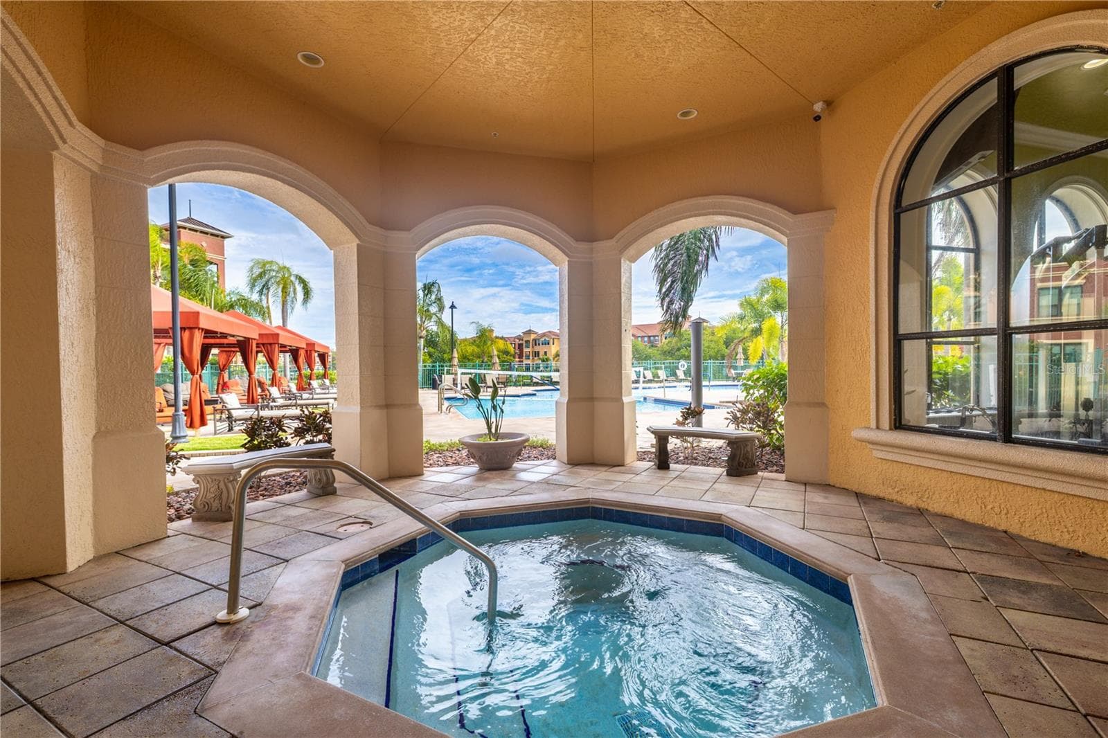 Covered heated spa area at the clubhouse featuring an inviting hot tub framed by elegant arches, with easy access to the resort-style pool deck and cabanas just beyond. - 2738 VIA TIVOLI #220B, CLEARWATER