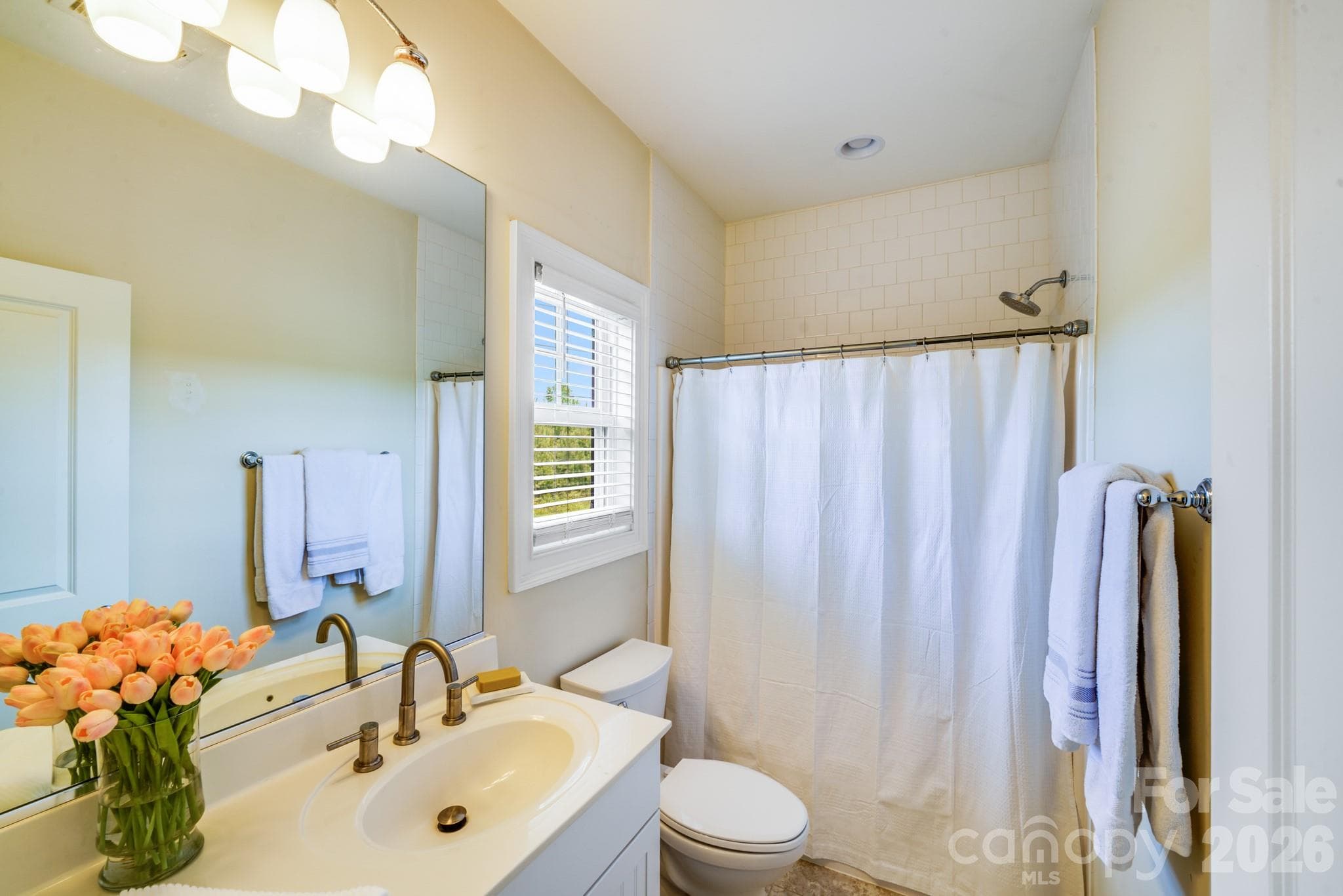 The private en-suite bath offers a bright and cheerful atmosphere with a large vanity, brushed nickel fixtures, classic tile surround, and a window for natural light and ventilation - 2702 Arsdale Road, Waxhaw