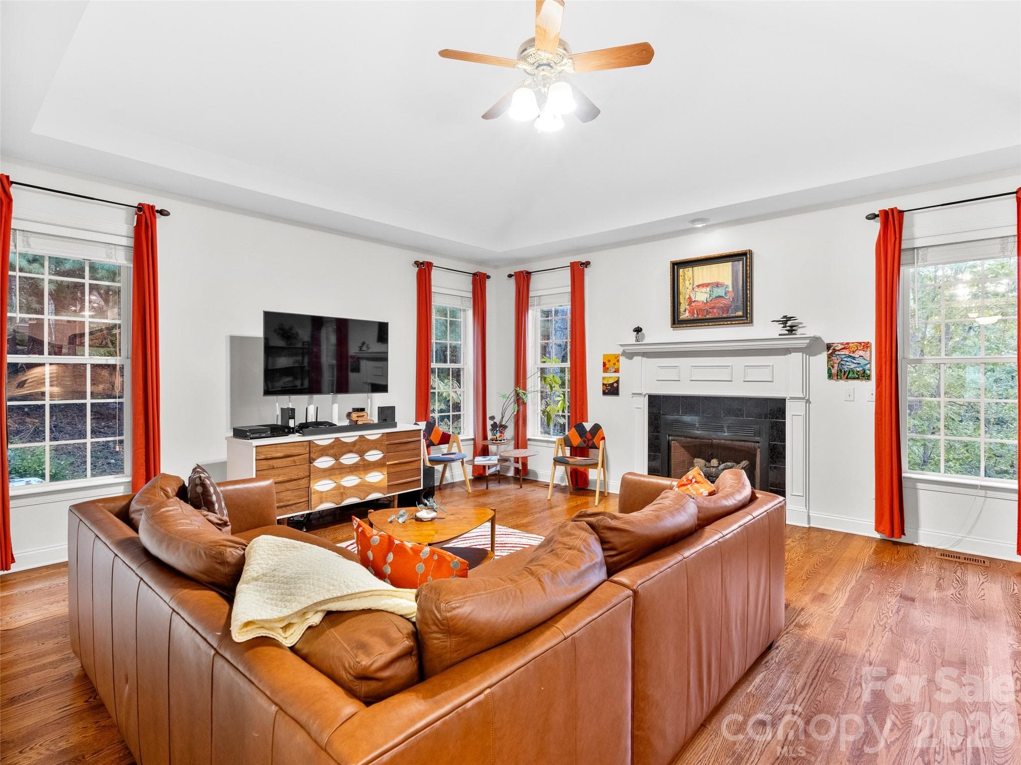 This family room features gleaming hardwood floors, a cozy gas fireplace, and abundant windows that fill the space with natural light, creating a welcoming spot for everyday living. - Asheville
