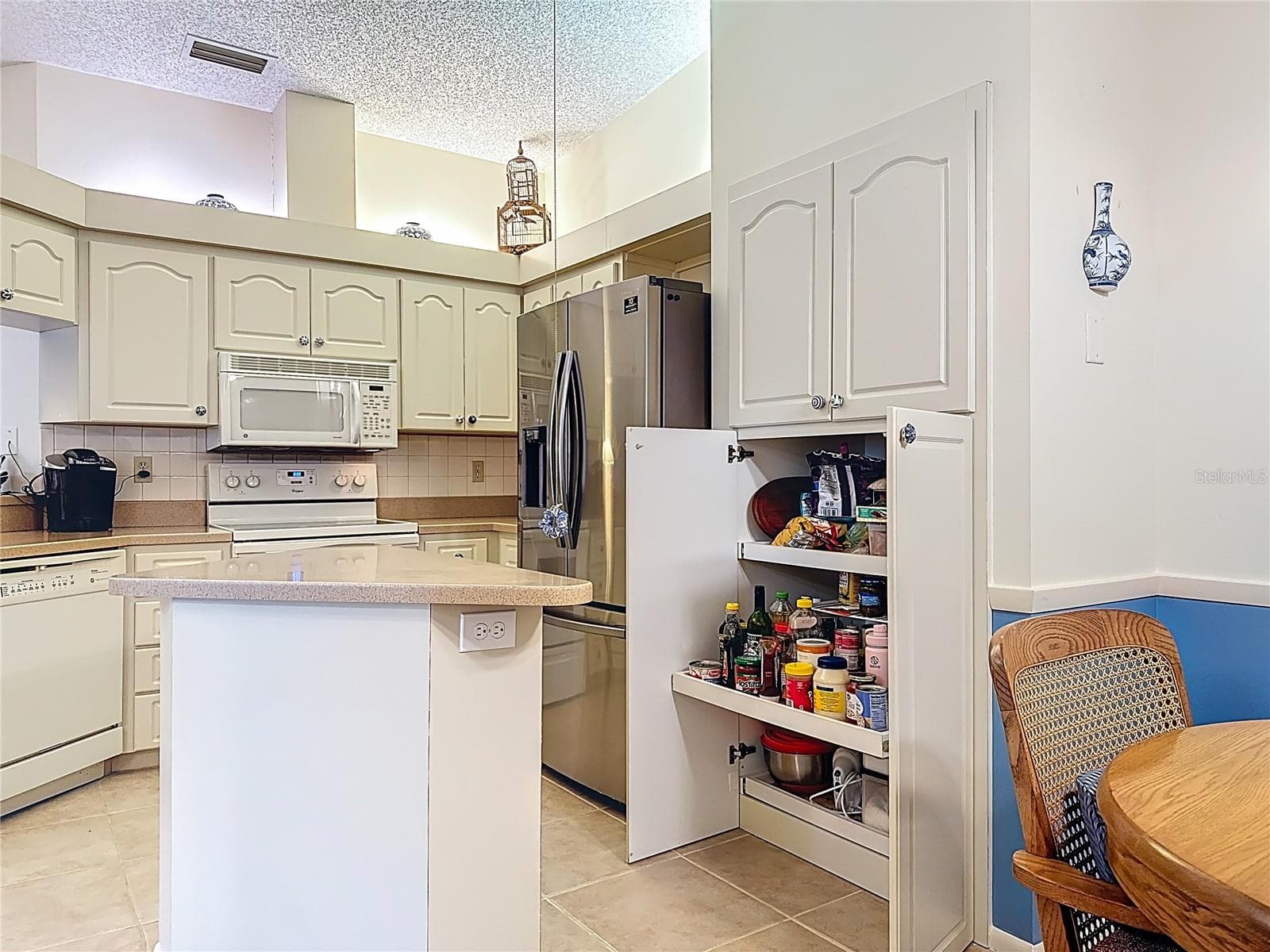 Kitchen pantry offers roll out shelving and an island. Stainless steel refrigerator (2024). - 5611 GARDEN LAKES DR, BRADENTON