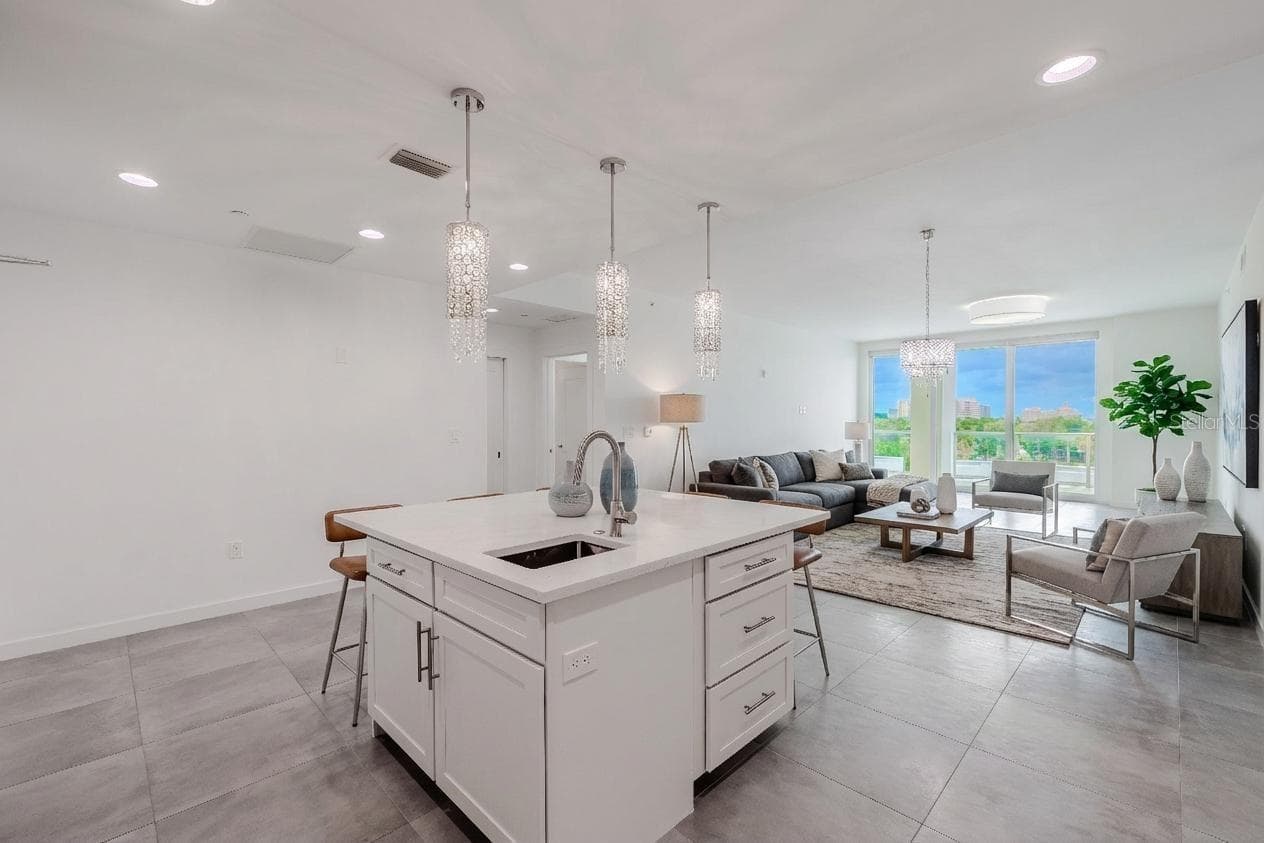 From the kitchen, enjoy an open-concept view that seamlessly connects the dining and living areas. Sleek tile flooring and designer lighting create a bright, contemporary flow, while floor-to-ceiling sliding glass doors frame lush treetop and skyline views beyond the spacious balcony - 920 N OSCEOLA AVE #703, CLEARWATER