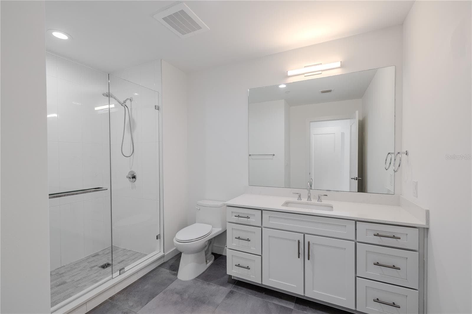 3rd bathroom Ensuite: The single vanity features shaker-style cabinetry with brushed nickel hardware, a sleek quartz countertop, and an oversized mirror with contemporary lighting above. Thoughtfully designed for both comfort and style, this ensuite combines modern elegance with everyday functionality — a private, polished extension of Bedroom 3. - 920 N OSCEOLA AVE #703, CLEARWATER