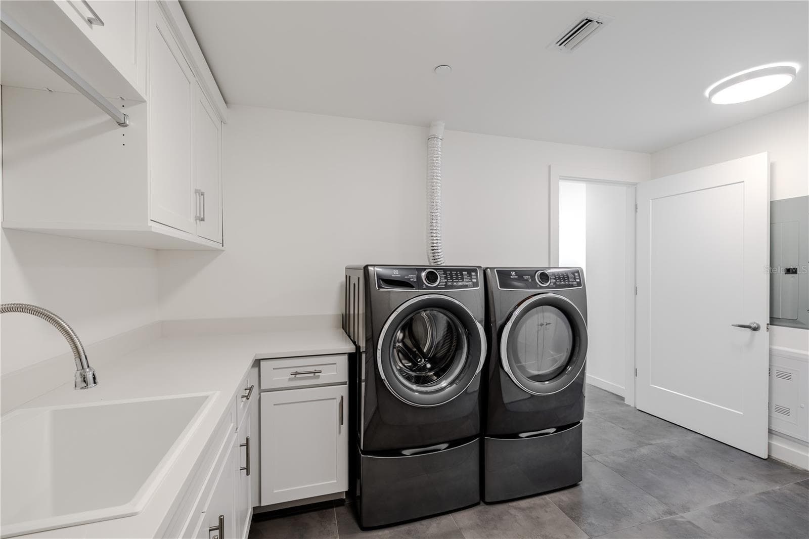 The beautifully designed laundry room features a sleek Electrolux front-load washer and dryer set, surrounded by abundant cabinetry and countertops for folding and organization. A deep utility sink and hanging rack add everyday convenience, while modern tile flooring and recessed lighting create a clean, contemporary look. Practicality meets style in this thoughtfully planned space. - 920 N OSCEOLA AVE #703, CLEARWATER