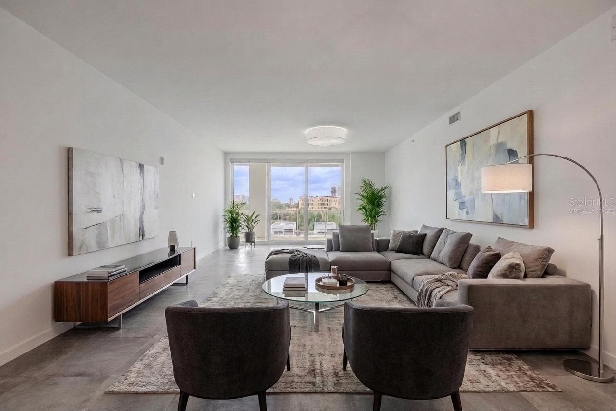 This bright and spacious dining and living area offers an elegant, open layout with sleek tile flooring and contemporary lighting. Floor-to-ceiling glass doors flood the space with natural light and open to a large balcony with sweeping water and skyline views. The modern chandelier adds a touch of sophistication, creating the perfect setting for entertaining or relaxing in style. Virtually staged photo. - 920 N OSCEOLA AVE #703, CLEARWATER