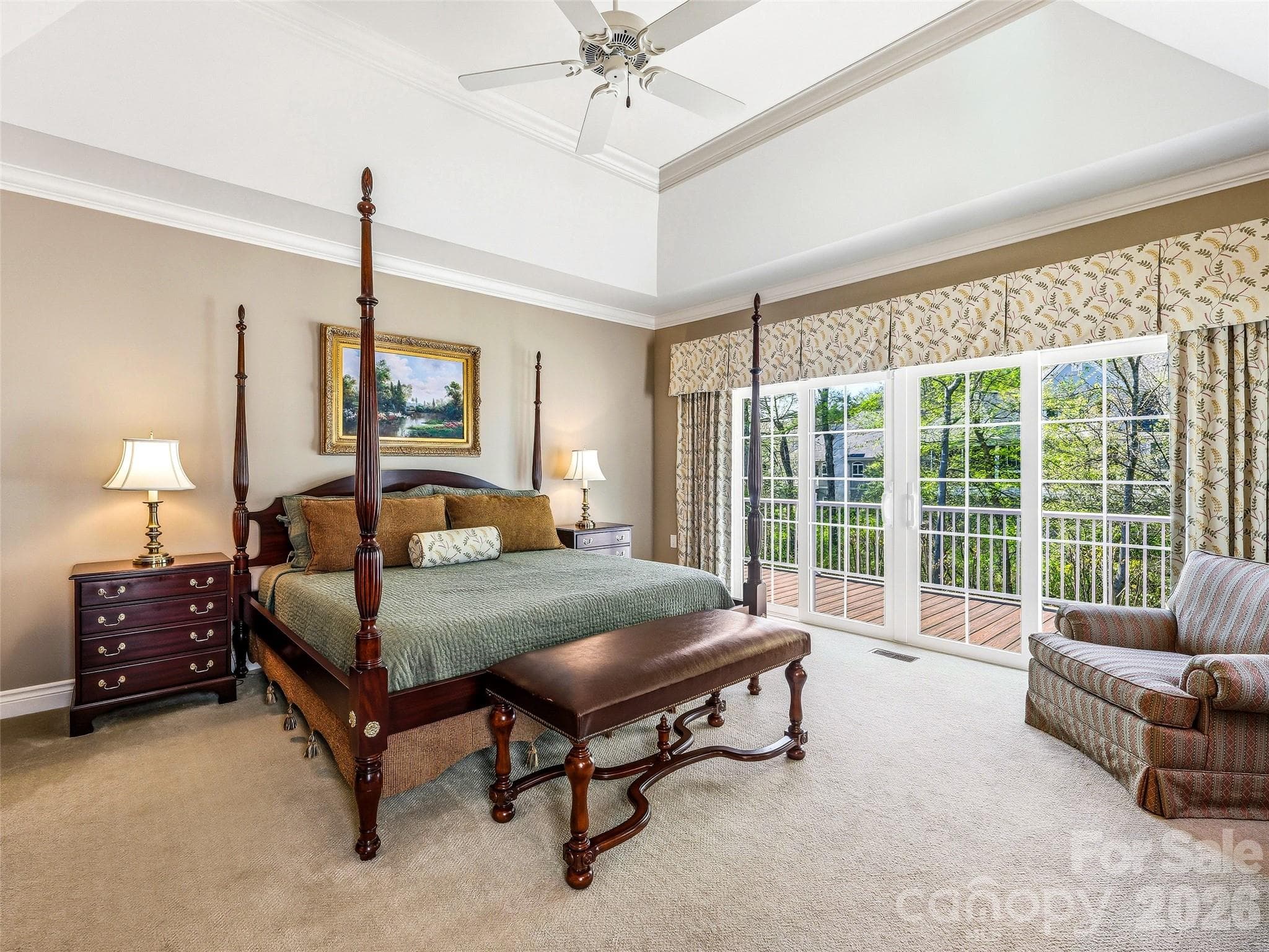 The spacious main level primary bedroom features a tray ceiling and sliding doors to the deck beyond. - 33 Tiverton Lane, Asheville