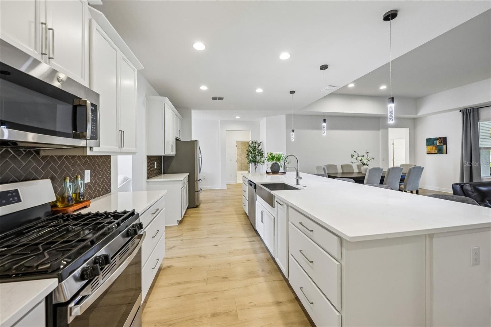 A massive QUARTZ ISLAND with bar seating sits beneath designer PENDANT LIGHTING, while STAINLESS STEEL APPLIANCES – including a GAS RANGE – pair perfectly with the stylish herringbone tile backsplash. - 6100 SIERRA CROWN ST, MOUNT DORA
