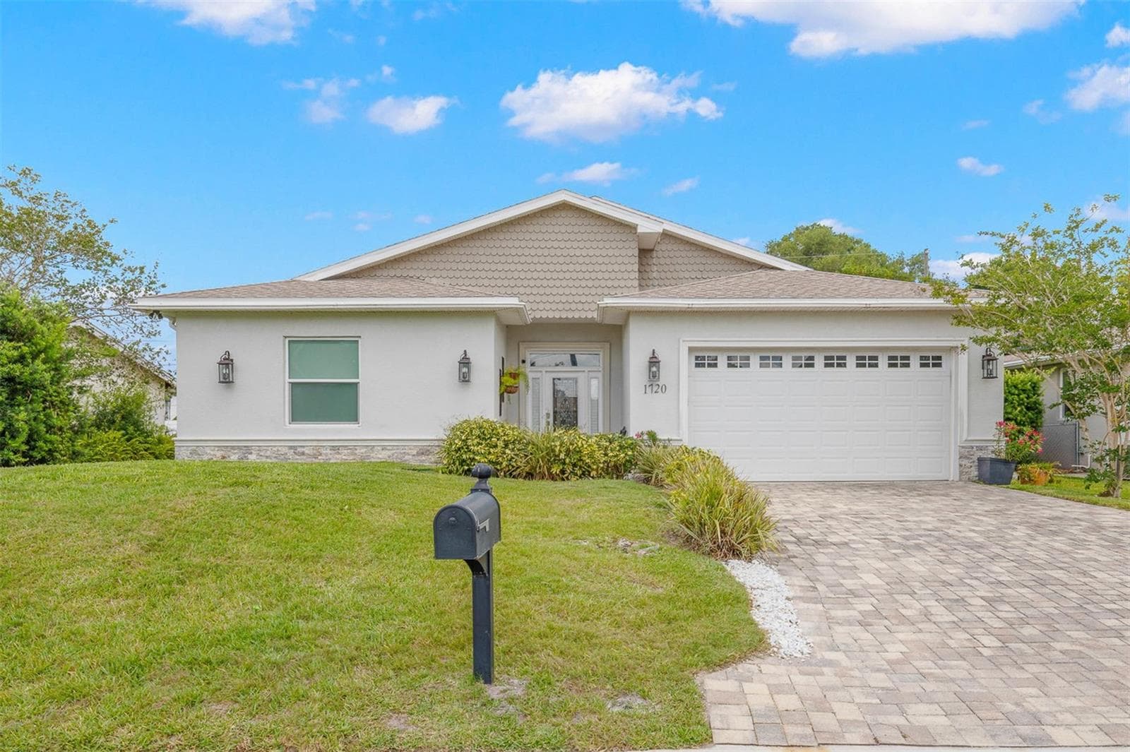 Contemporary coastal styling meets quality construction in this beautifully finished residence featuring a brick paver driveway, oversized 2-car garage, manicured landscaping, decorative exterior lighting, and a welcoming covered entry with leaded glass front door and sidelights. - 1720 VERDE DR, CLEARWATER