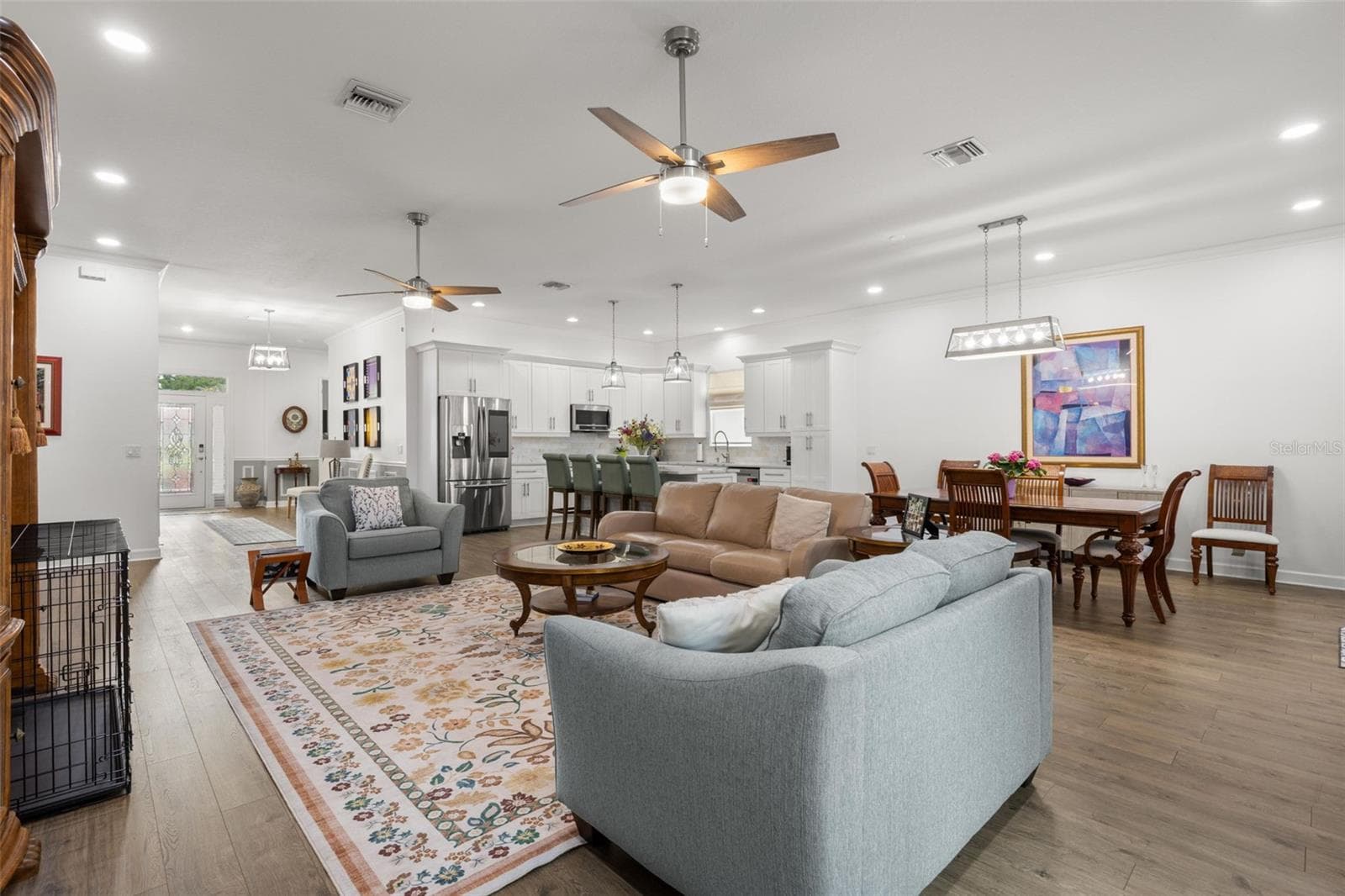 The open great room layout offers generous living and dining spaces beneath high ceilings with crown molding, recessed lighting, and dual contemporary ceiling fans. Wide-plank luxury vinyl flooring carries throughout the main living areas, while the oversized kitchen island creates a natural centerpiece for gathering and conversation. - 1720 VERDE DR, CLEARWATER