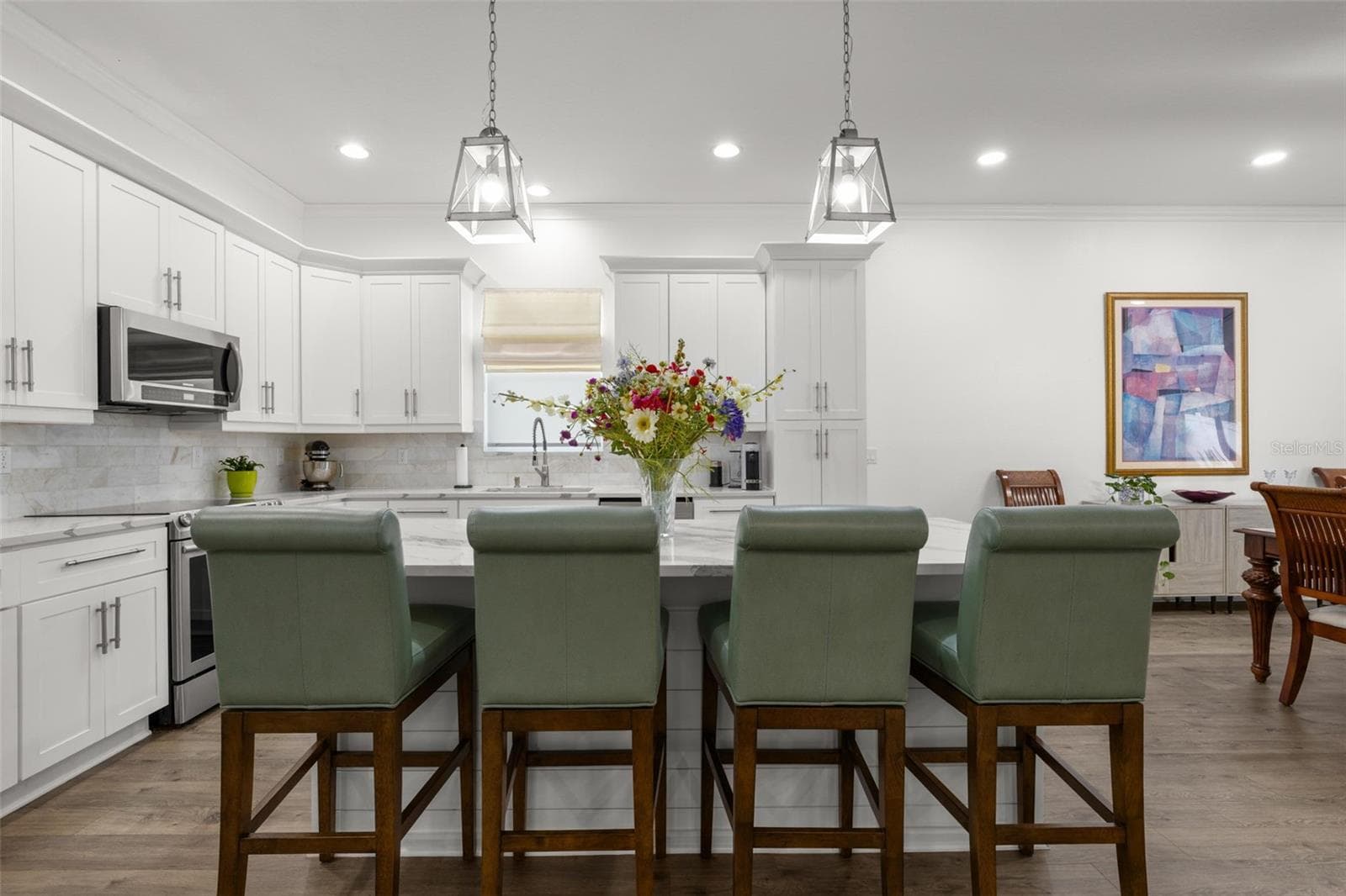 The oversized center island provides extensive prep space, additional storage, integrated microwave, and comfortable seating beneath contemporary pendant lighting. Crisp white shaker cabinetry with crown molding, designer quartz countertops, upgraded stainless appliances, recessed lighting, and an elegant onyx marble backsplash create a clean, sophisticated kitchen design. - 1720 VERDE DR, CLEARWATER