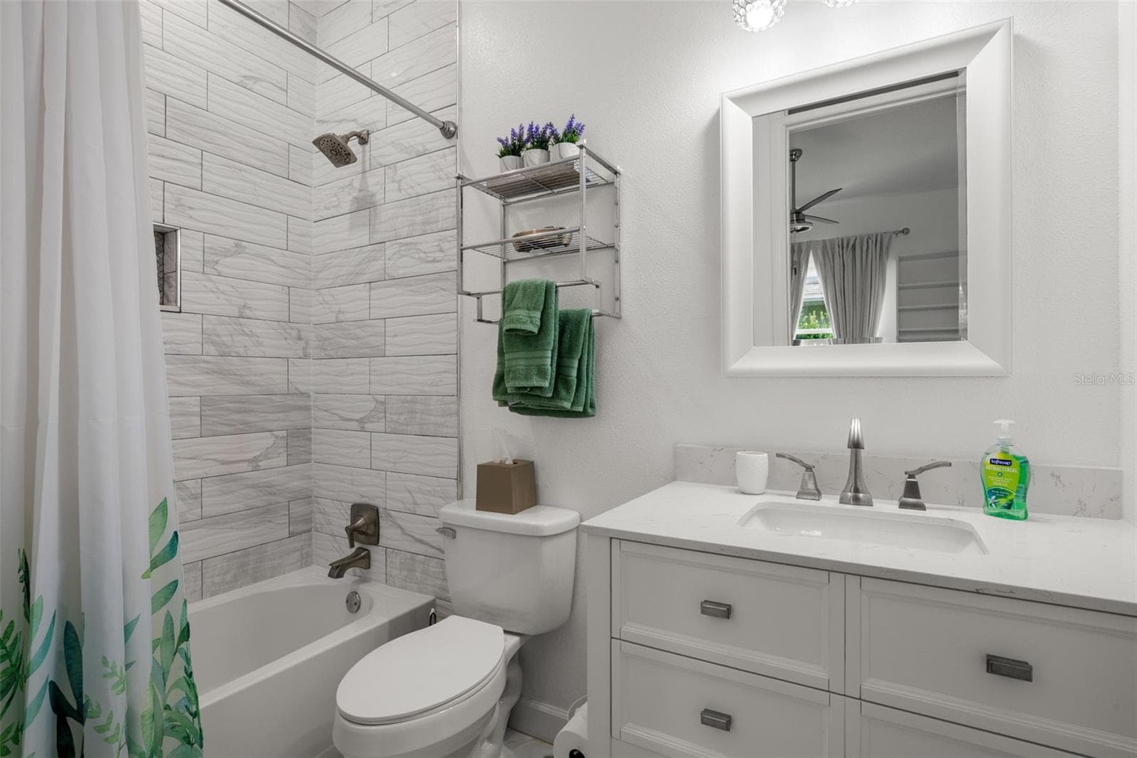 Bedroom 3 ensuite bath features a tub with shower, marble-look tile extending to the ceiling, a mirrored vanity with quartz countertop, upgraded fixtures, and a built-in shower niche. - 1720 VERDE DR, CLEARWATER