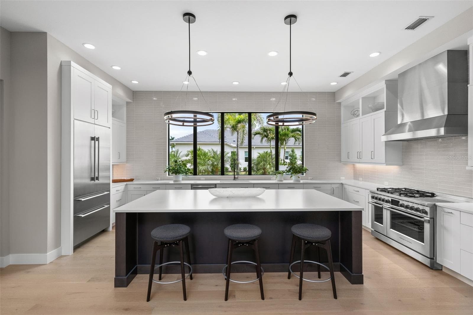 Matte-finished quartz countertops, a large center island with seating, tile backsplash, wood cabinetry with display shelving and pendant lighting create a polished and inviting atmosphere. - 11721 RIVE ISLE RUN, PARRISH