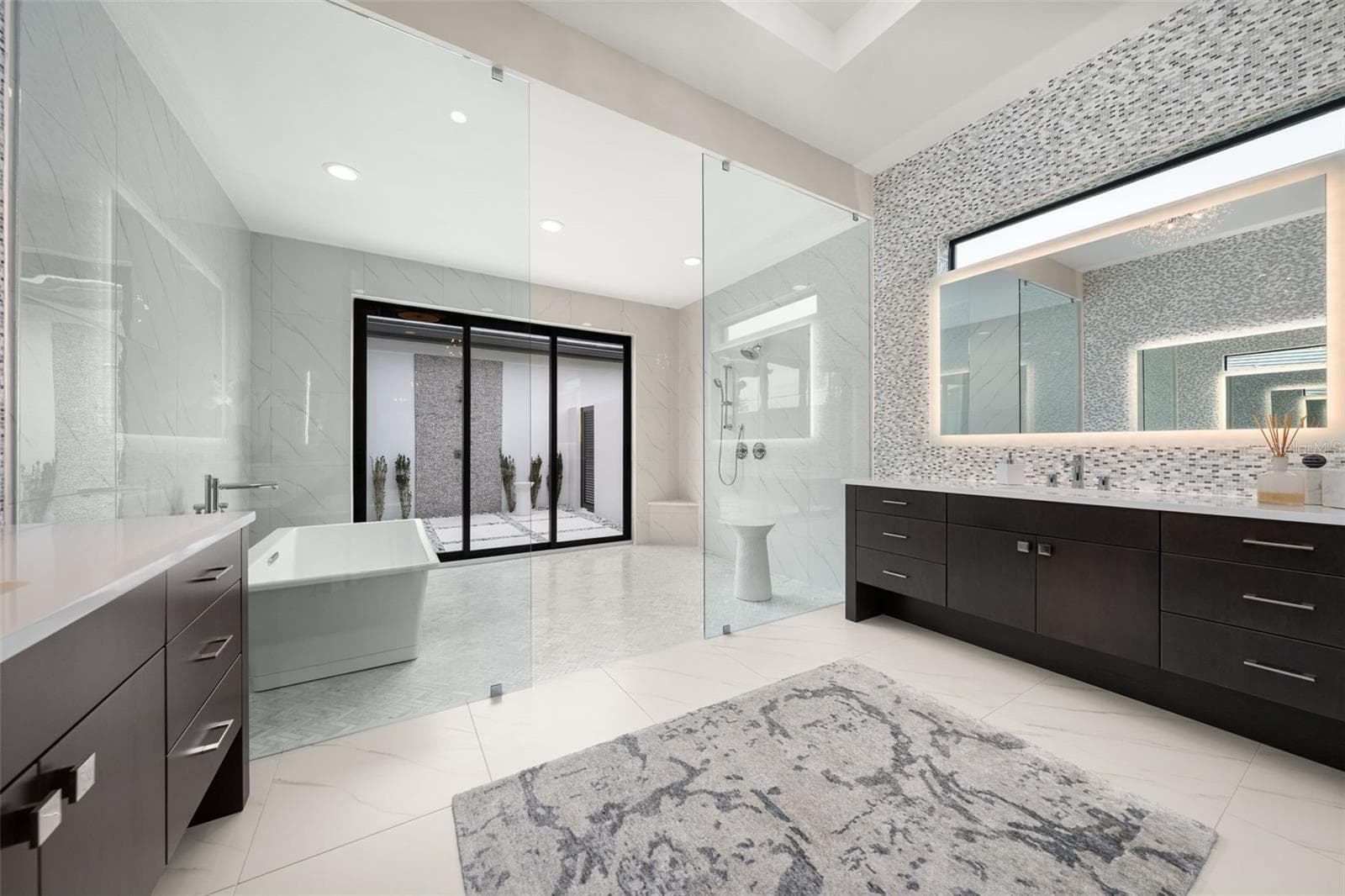 It features dual expansive vanities, square sinks, custom tile backsplash, backlit mirrors with integrated TV feature. - 11721 RIVE ISLE RUN, PARRISH
