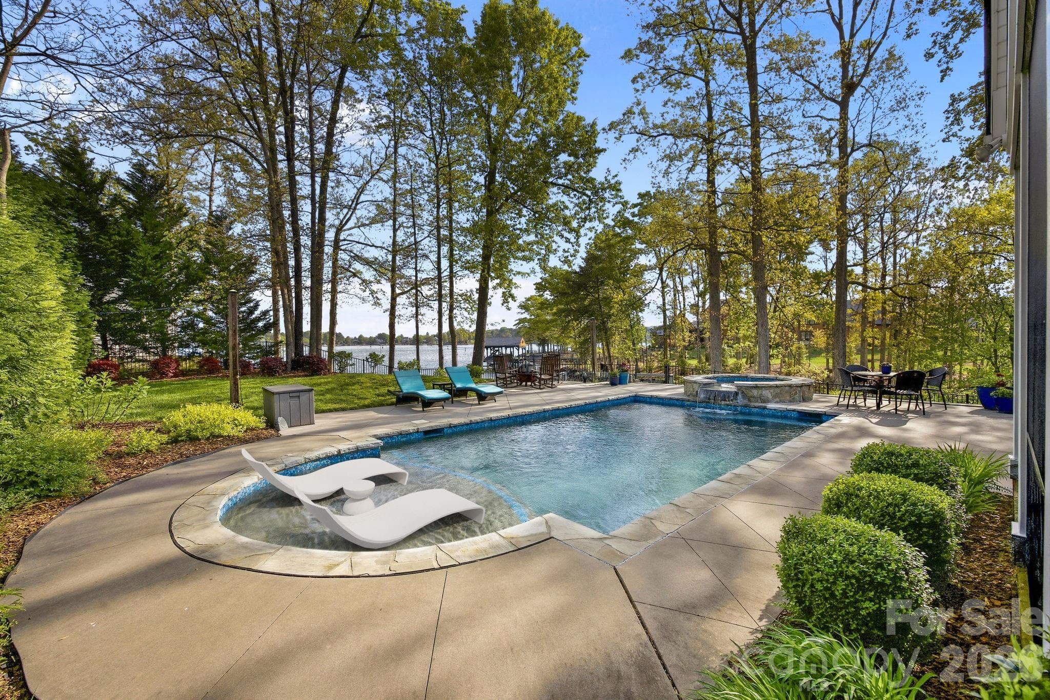 Private backyard features an in-ground pool with sun shelf, spa, expansive patio, and mature trees with water views. - Cornelius