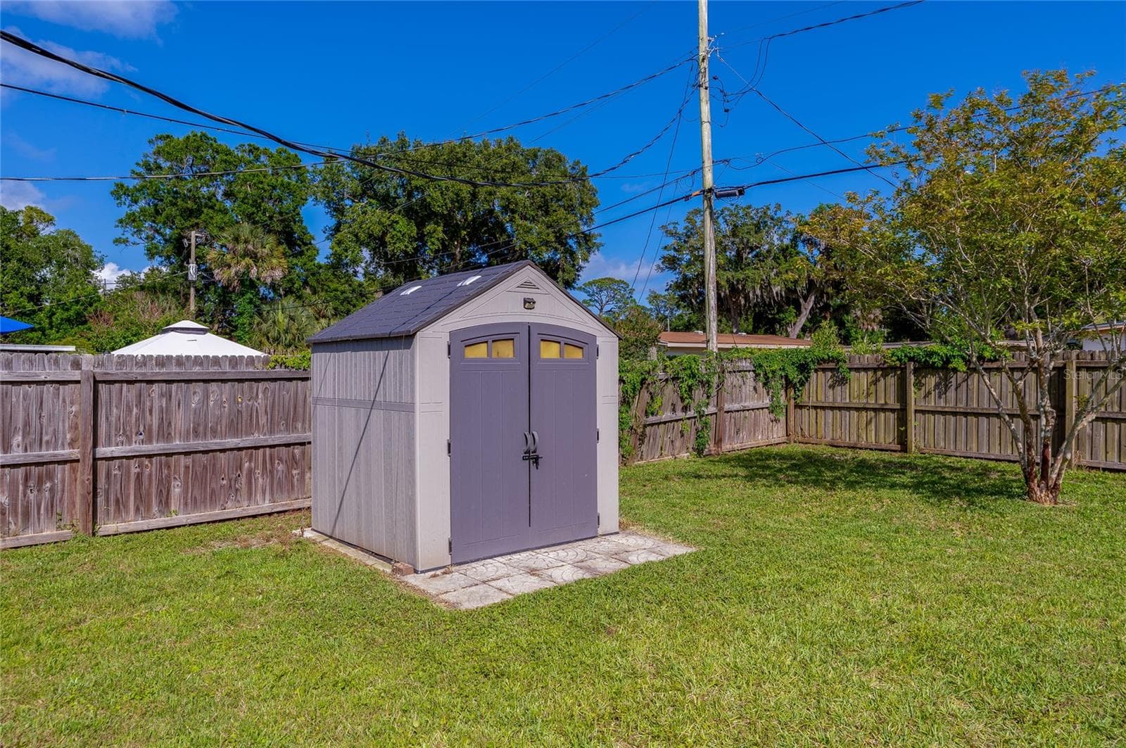 Fully fenced backyard featuring a spacious, modern storage shed set on a paved foundation. - 723 STEELE AVE, SOUTH DAYTONA