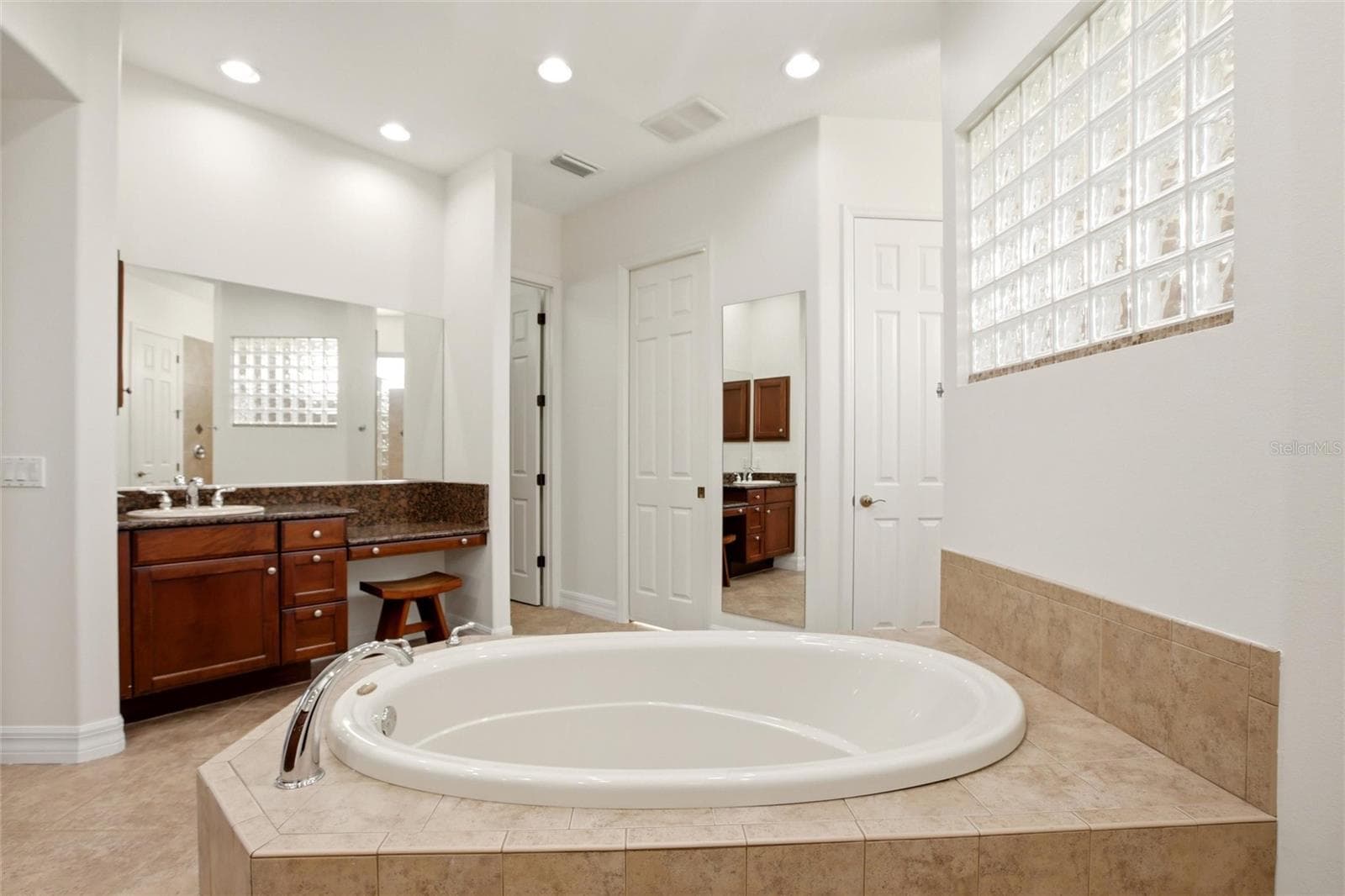 The primary bathroom features a soaking tub, split vanities with dedicated makeup counter space, a spacious walk-in shower with dual shower heads, a private water closet, and dual walk-in closets with custom organization. - 8417 LONE EAGLE WAY, SARASOTA