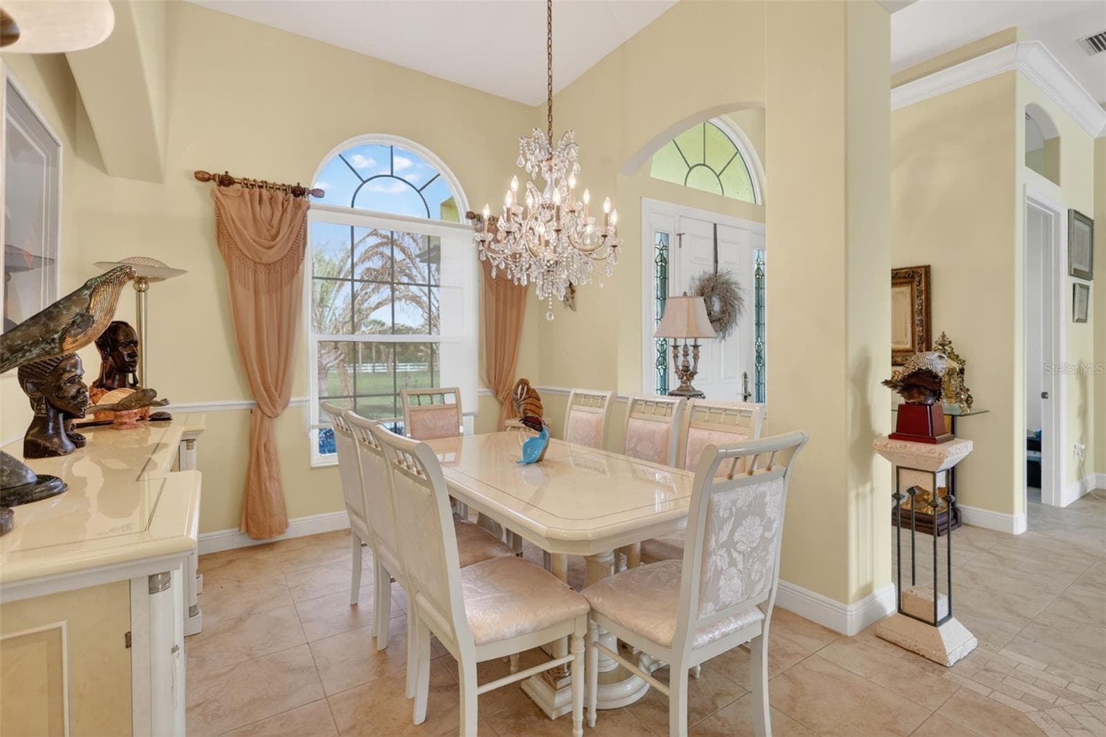 Elegant formal dining room featuring soaring ceilings, crown molding, abundant natural light, and a statement chandelier for memorable gatherings and entertaining. - 1210 408TH CT E, MYAKKA CITY