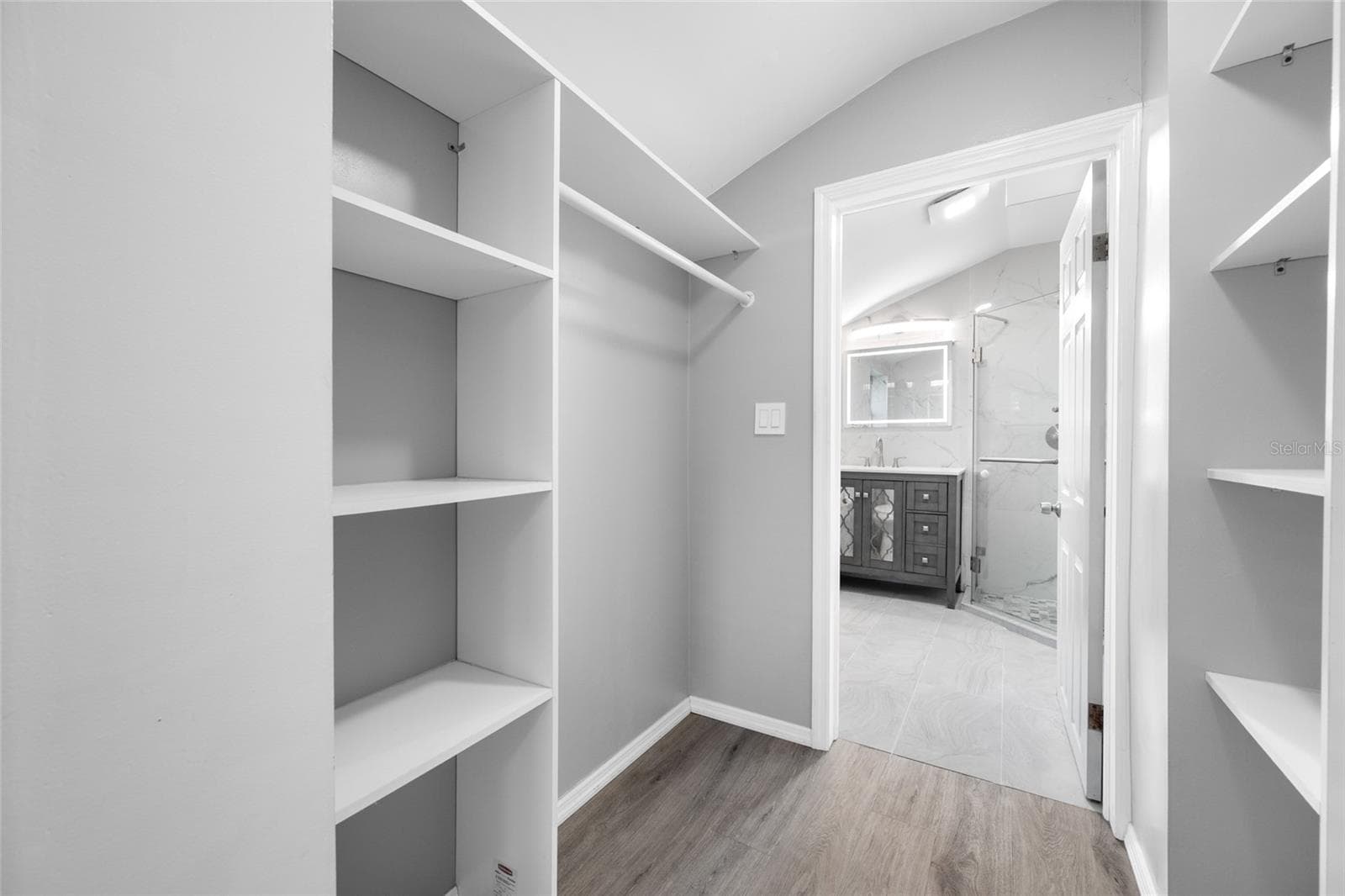 Primary Bedroom suite with walk-in closet, with built in shevles, that opens through to private en-suite updated bathroom with marble tile and glass shower. - 5044 BETTY ST N, ST PETERSBURG